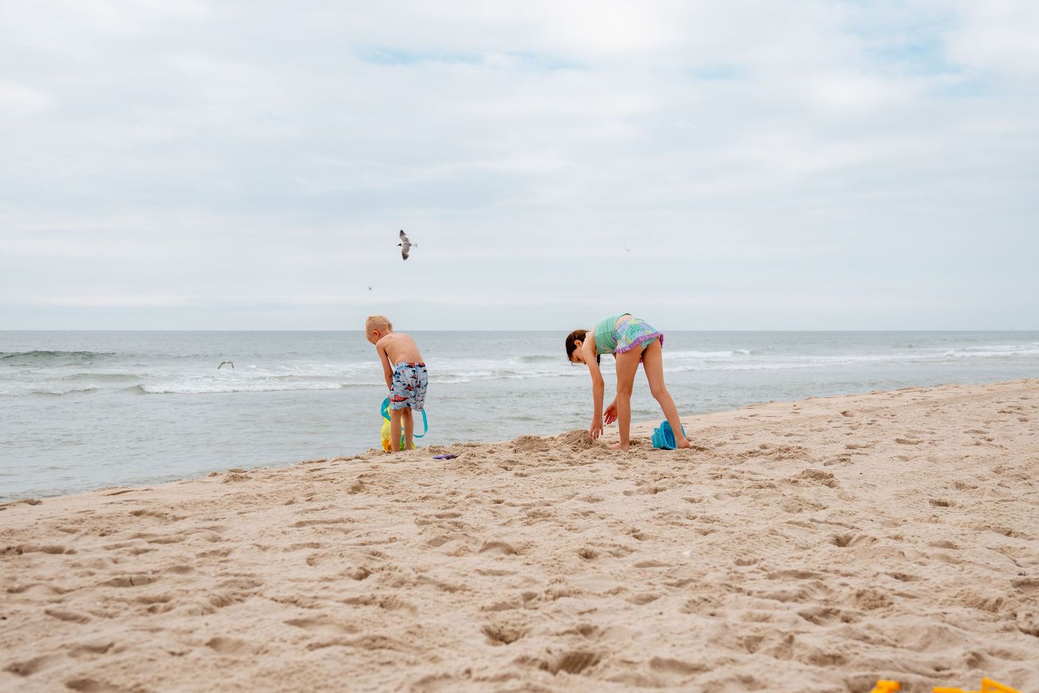 Two children playing in the sand on a beach near the ocean on a cloudy day.