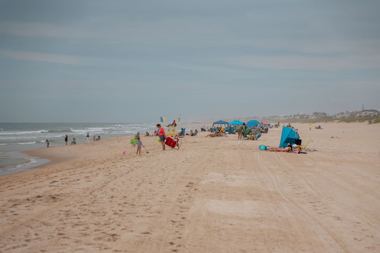 Beachgoers relax on a sandy shore with colorful umbrellas and tents on a cloudy day.