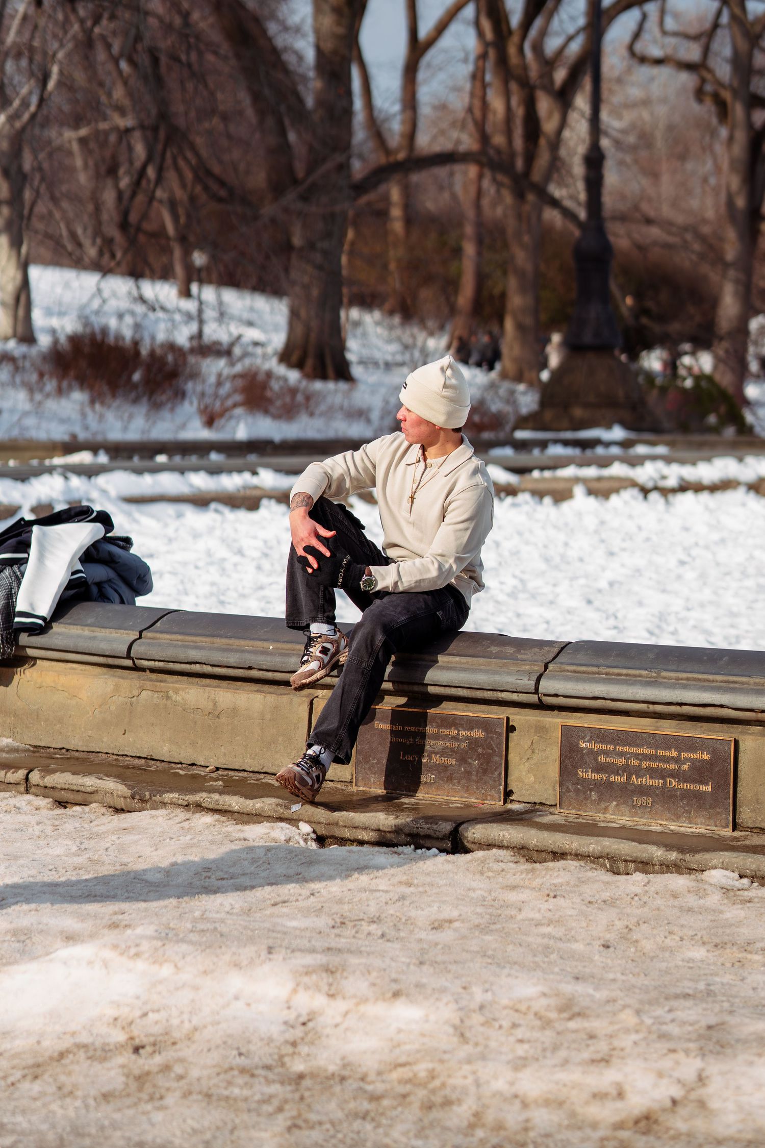 Man sitting on snowy park bench in Central Park wearing rollerblades on a cold winter day.