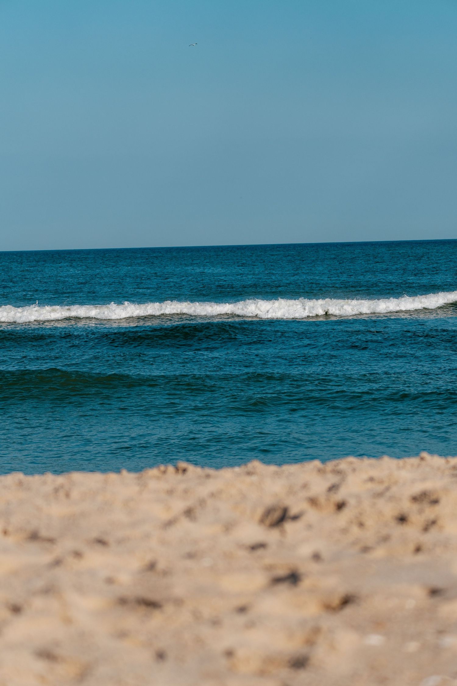 Turquoise ocean waves breaking onto a sandy beach under a clear blue sky on a sunny day.