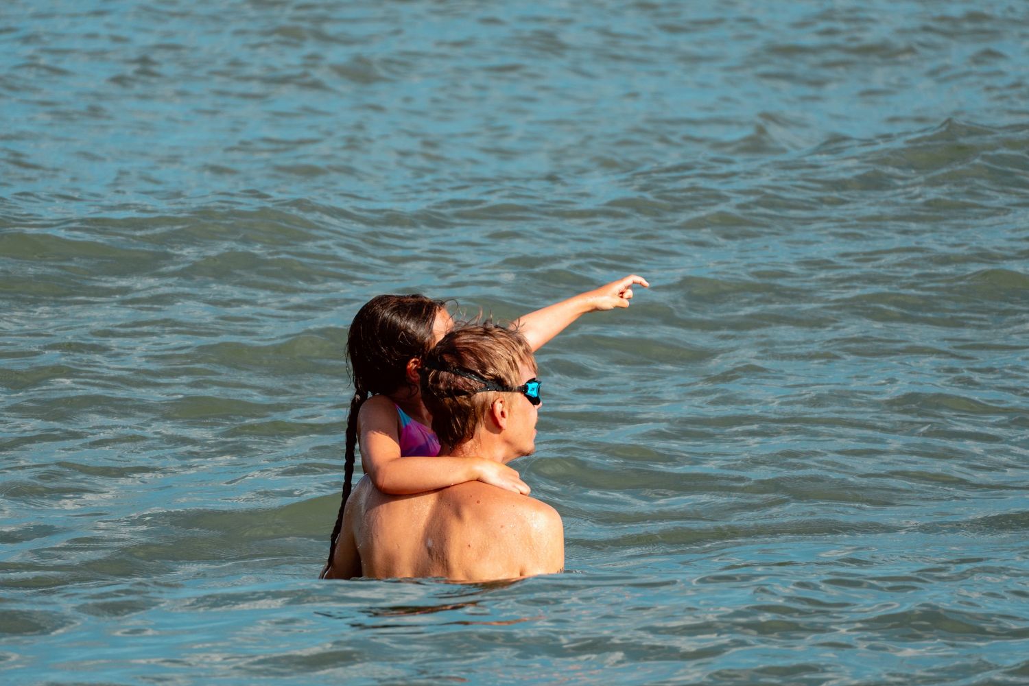 Two people embracing in ocean water, one pointing into the distance on a sunny day.