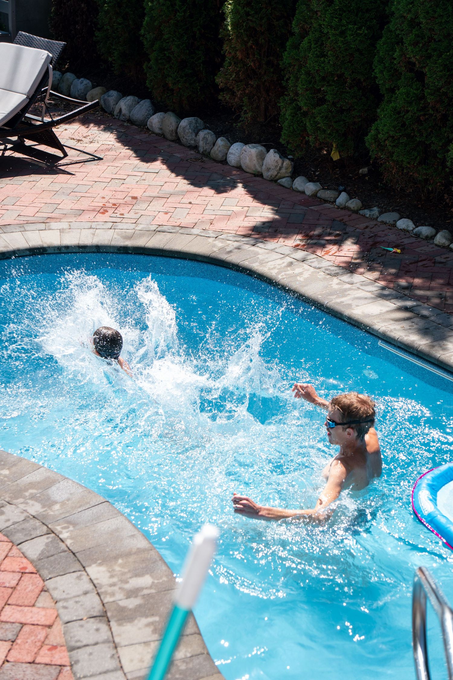 Two swimmers splash energetically in a bright blue backyard swimming pool.