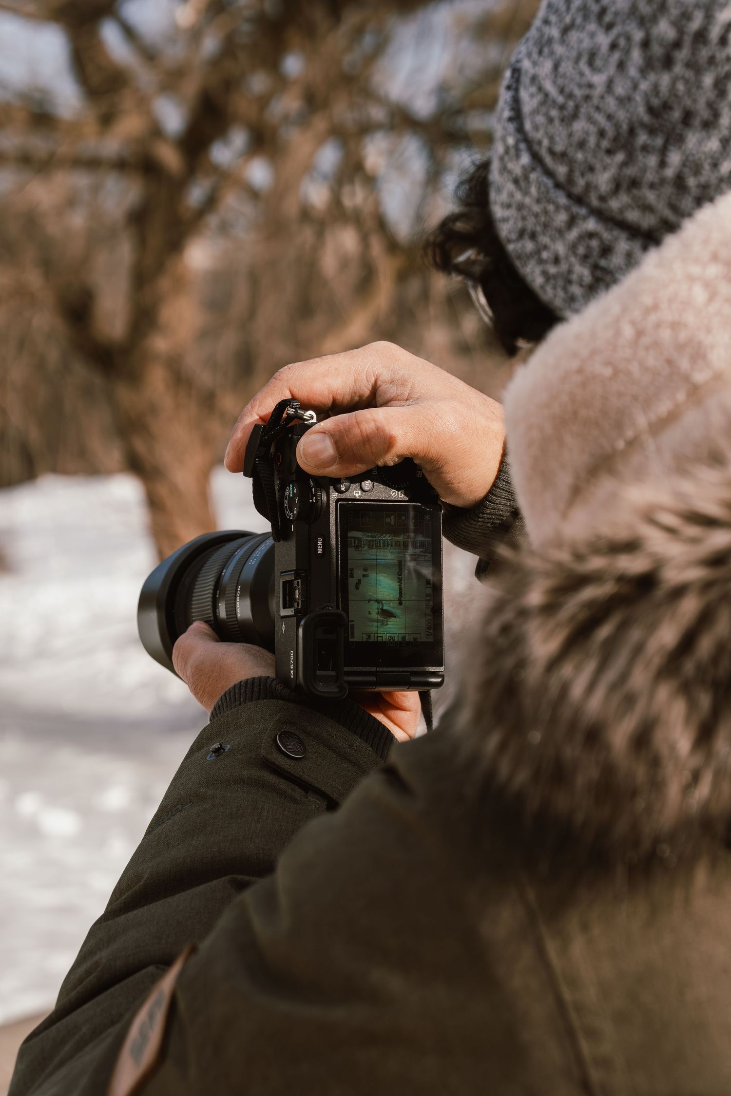Close-up of hands holding a DSLR camera with tilting LCD screen in a winter outdoor setting with snow.