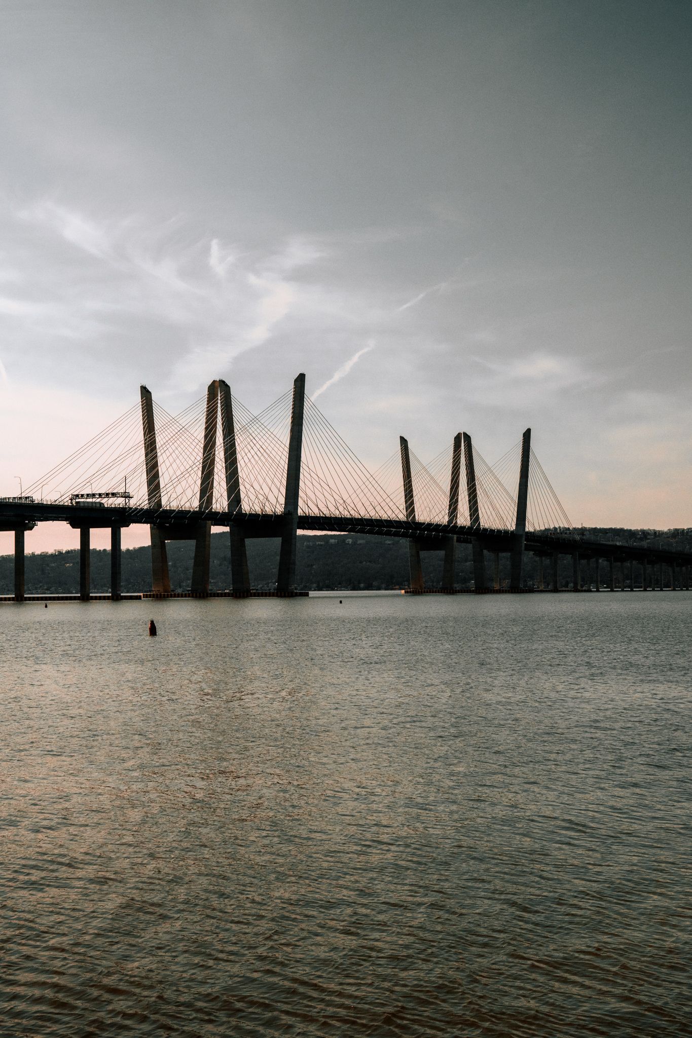 A dramatic cable-stayed bridge silhouetted against a cloudy sunset sky reflecting on calm river waters.