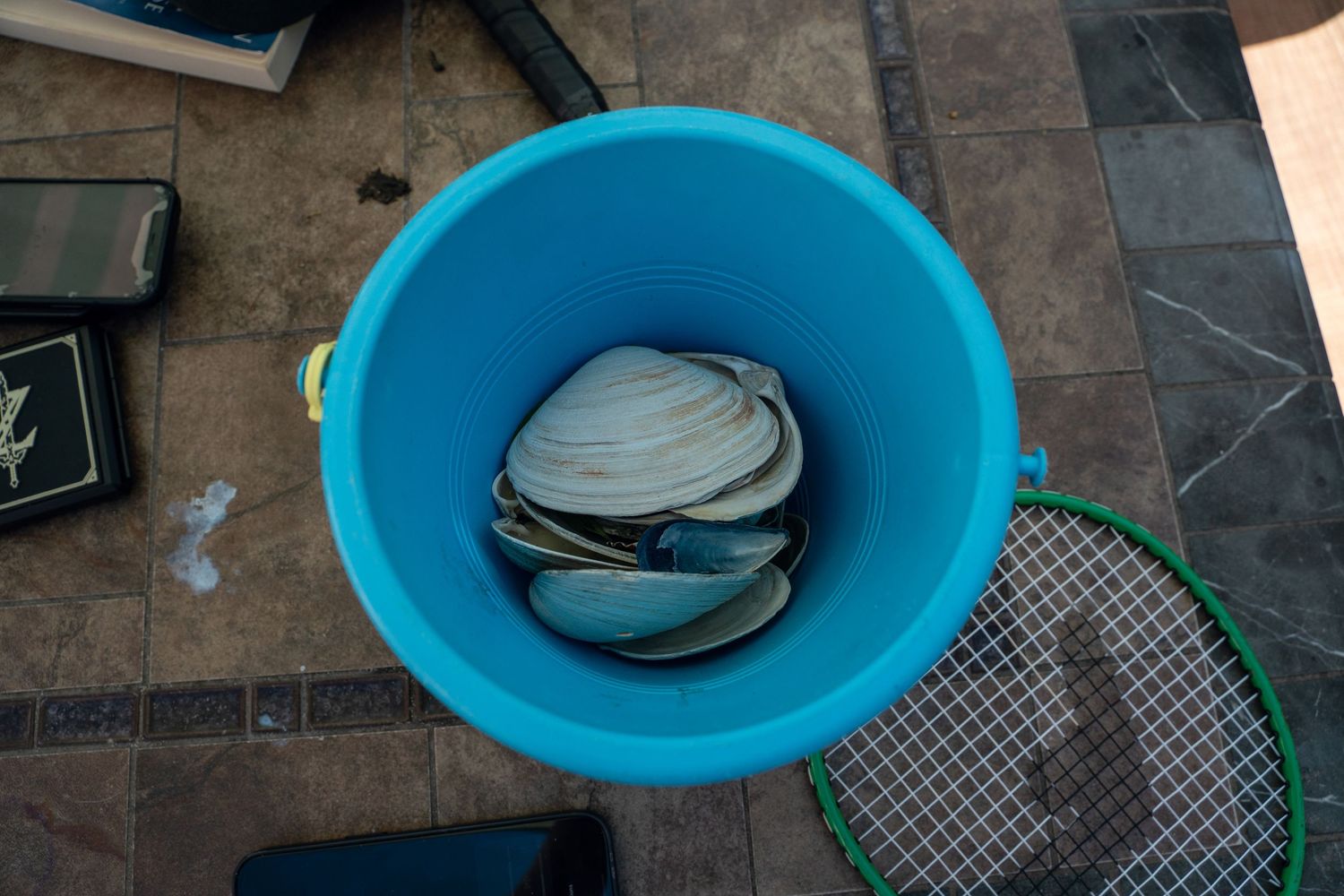 Top view of a turquoise bucket filled with colorful flip flops on a patio floor.