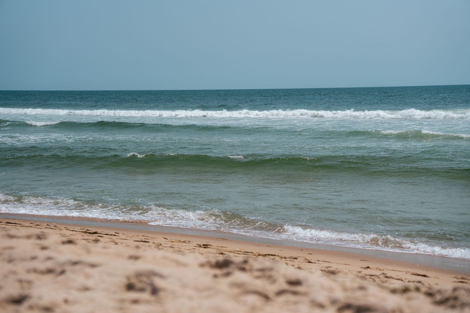 Sandy beach with gentle ocean waves rolling ashore under a clear sky, showcasing serene coastal scenery.