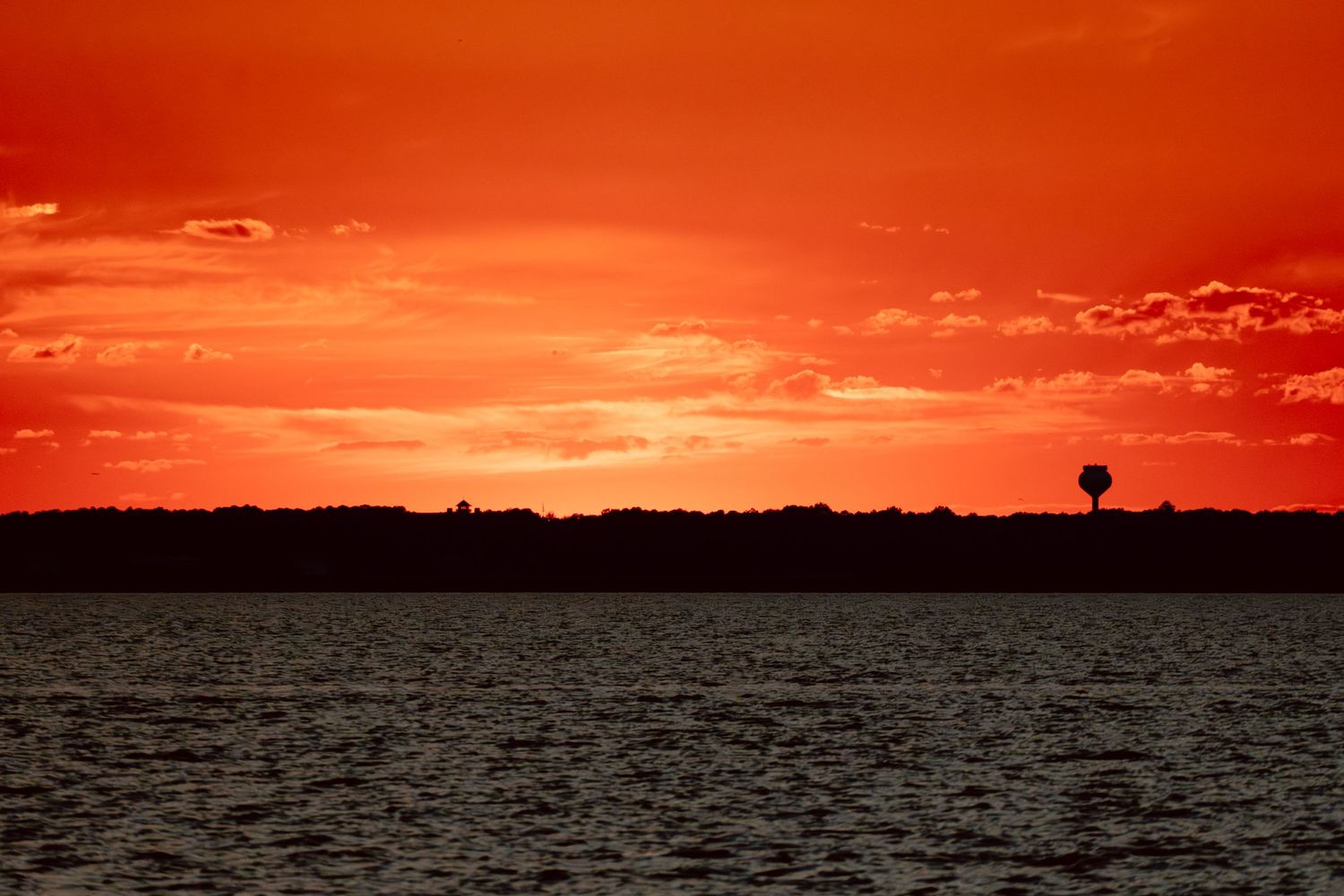 Stunning fiery red and orange sunset sky reflecting over a calm lake with a silhouetted shoreline.