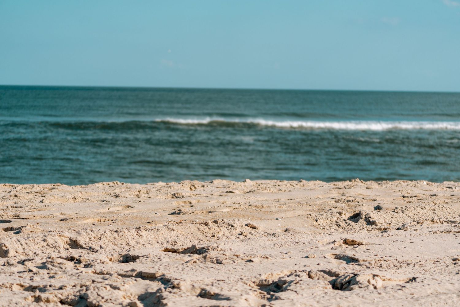 A serene sandy beach with gentle ocean waves and a clear blue sky on a sunny day.