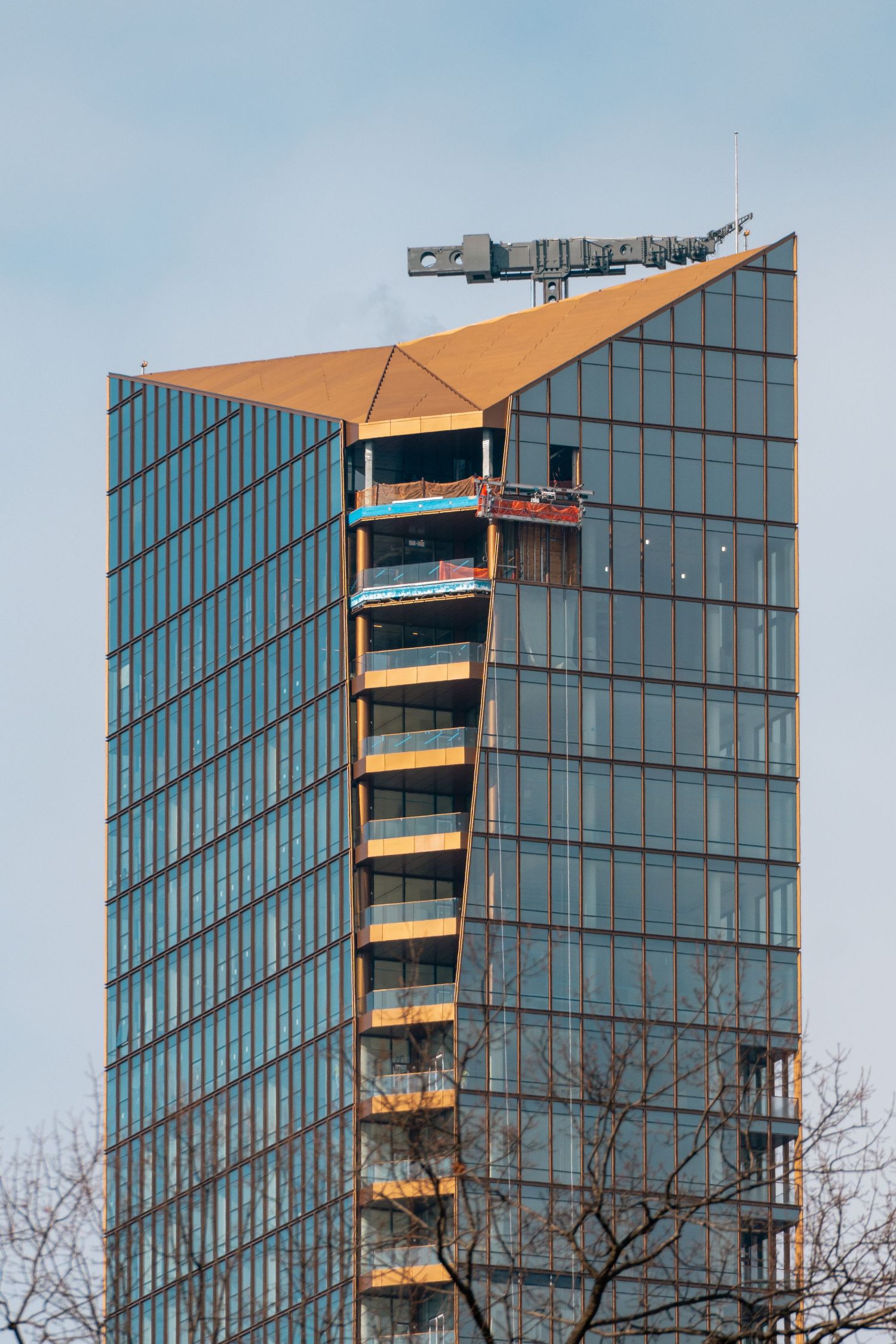 Modern glass skyscraper with distinctive angular copper-toned facade detail against a blue sky.