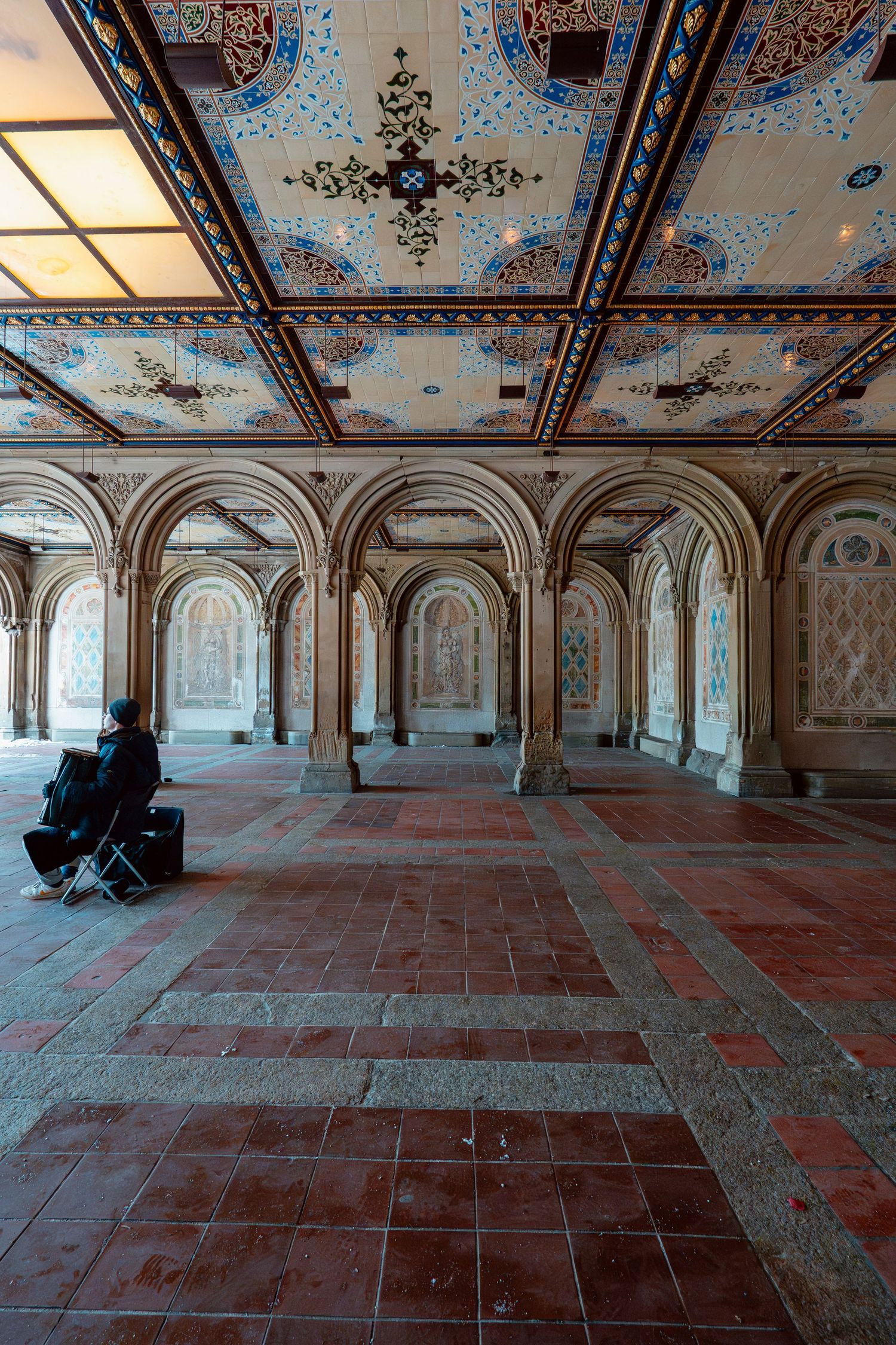 A lone visitor sits inside the elaborately decorated Bethesda Terrace arcade with colorful tiled ceiling.