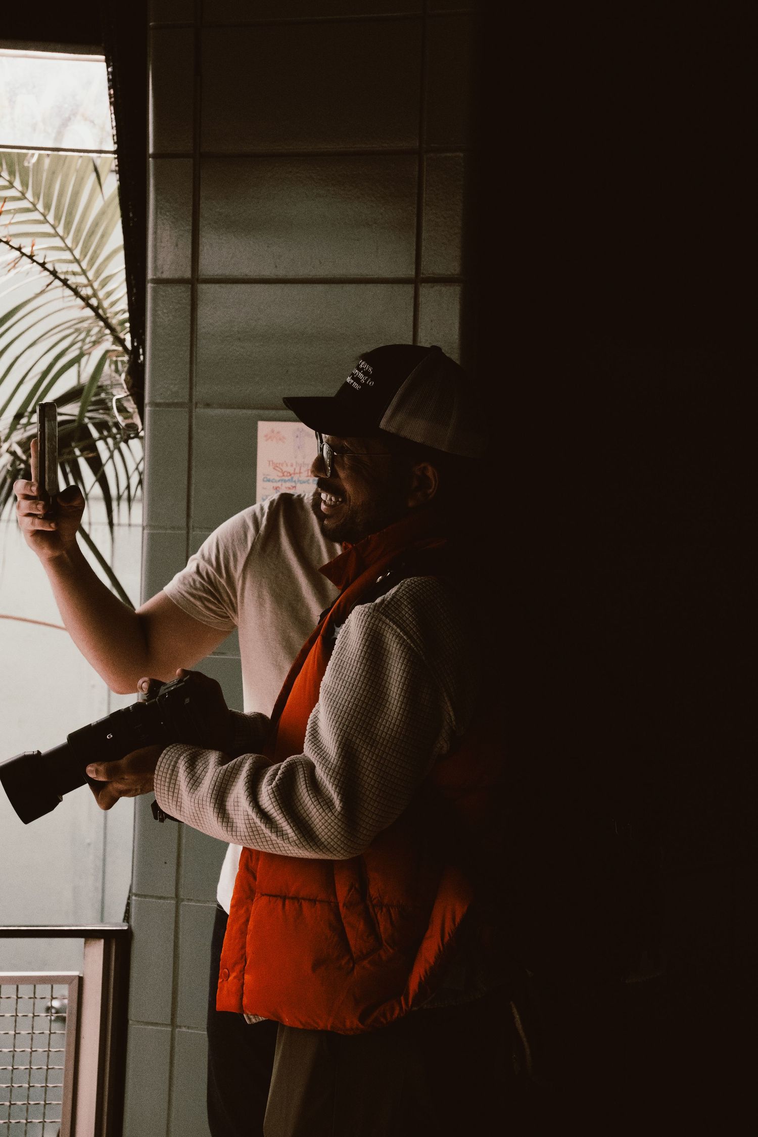 A photographer in an orange vest and cap holding a camera in a dimly lit space.