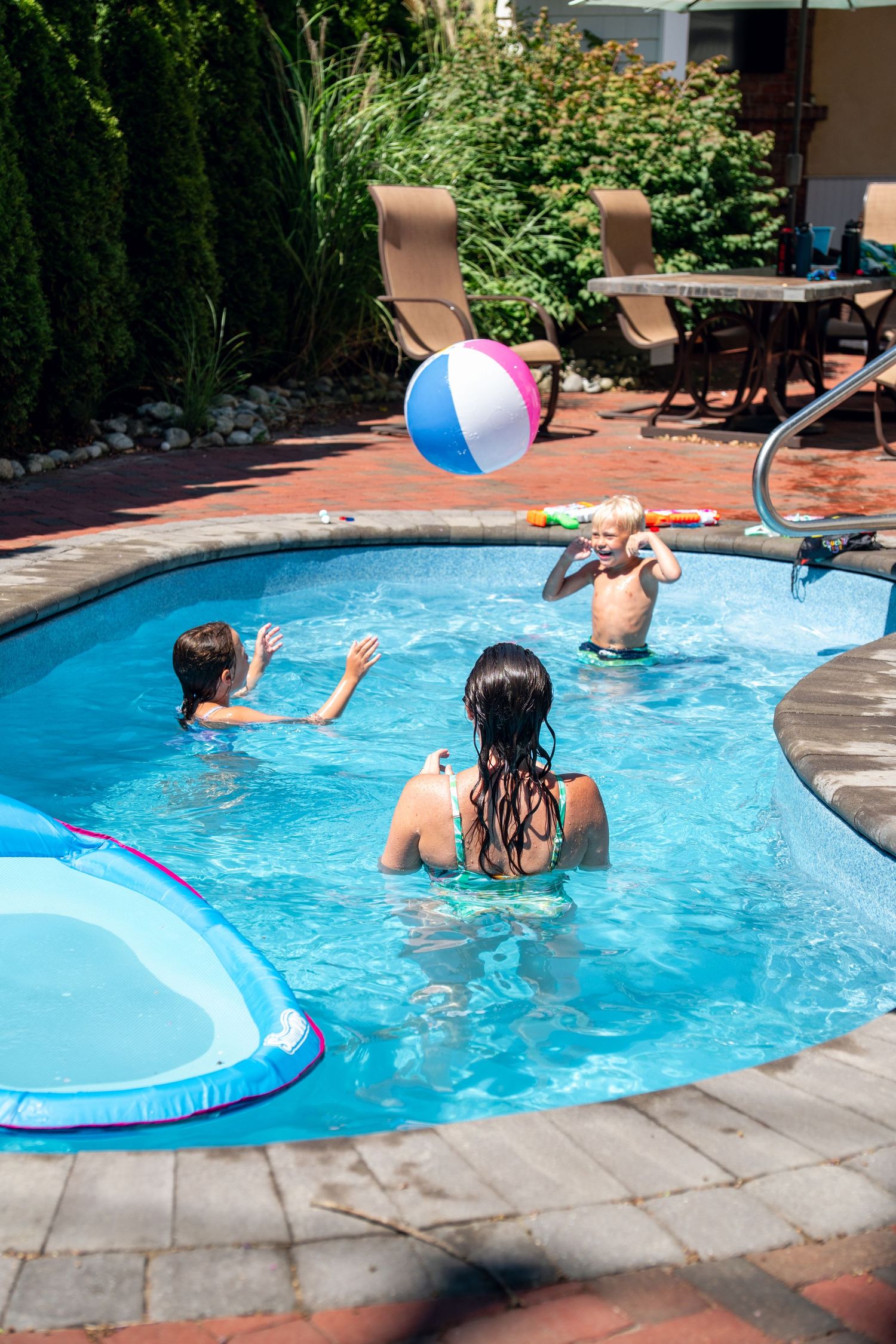Two people playing with a beach ball in a backyard swimming pool on a sunny day.