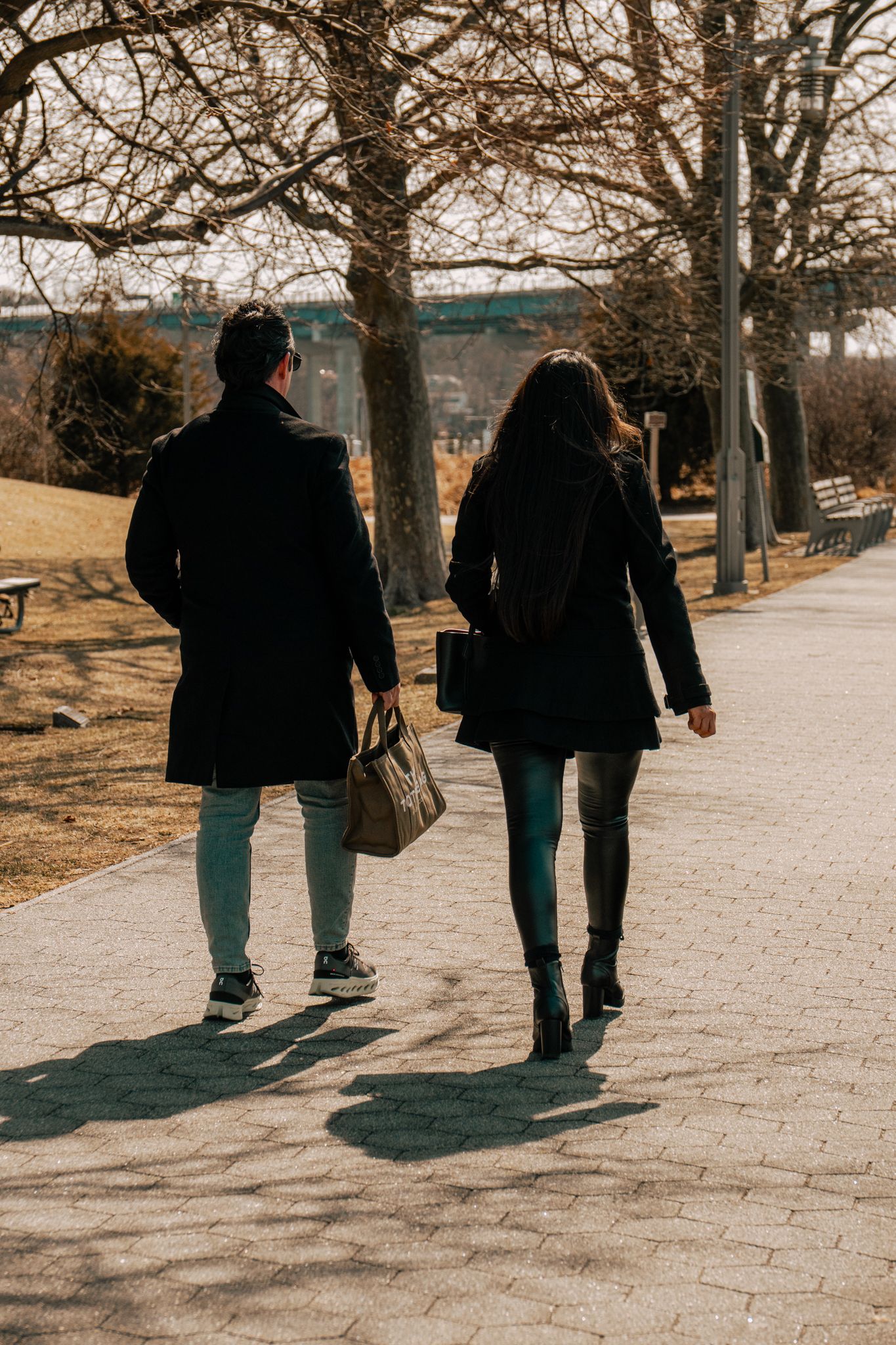 Couple walking away on brick park path lined with bare trees in winter.