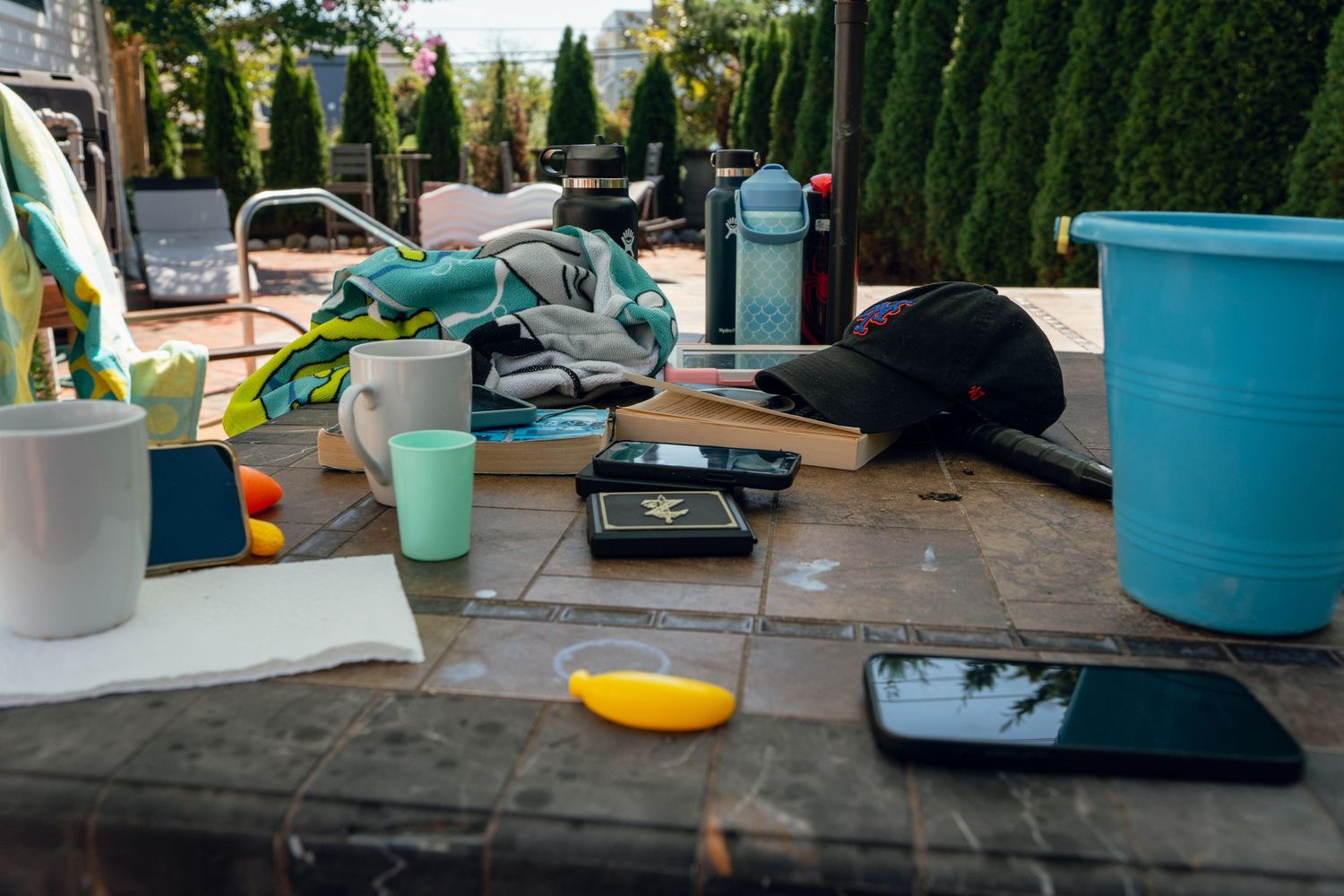 Cluttered outdoor patio table with phone, books, water bottle, and various items.