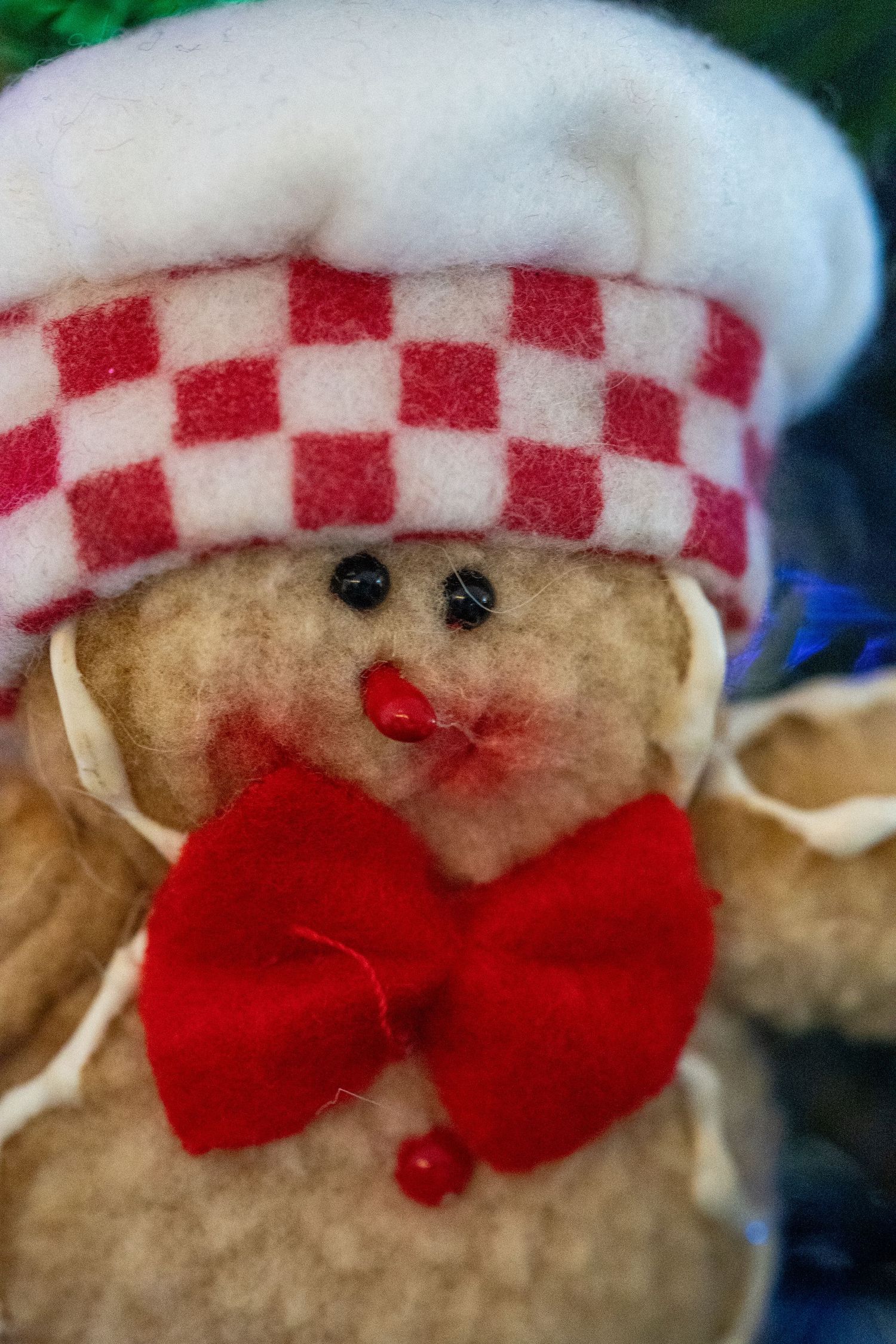 A festive gingerbread man plush toy wearing a checkered chef hat and red bow tie.