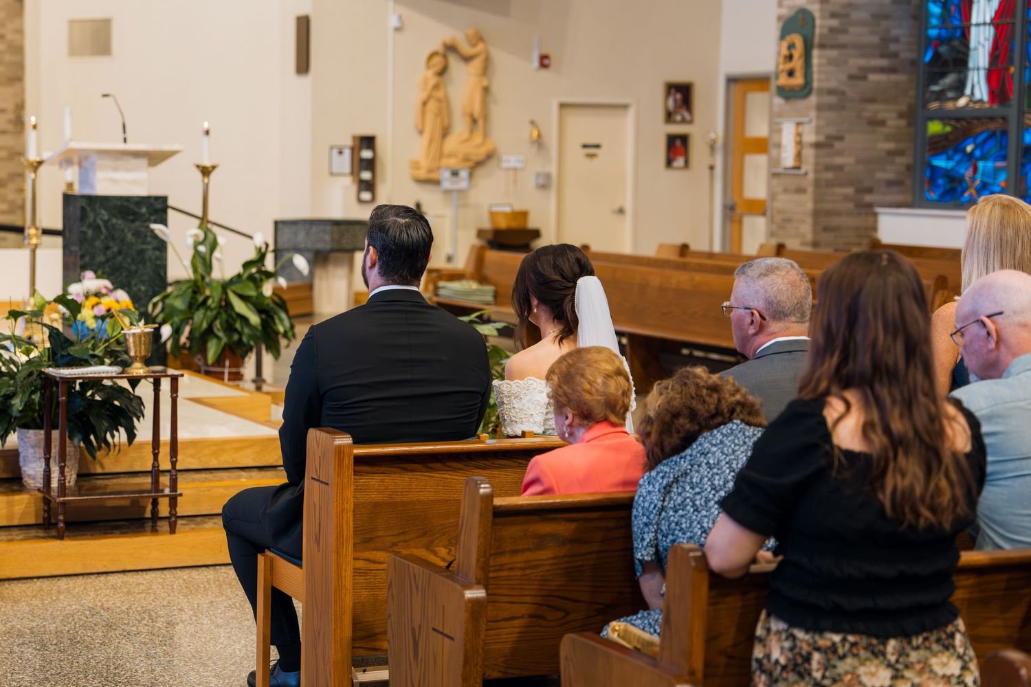 Guests seated in wooden church pews during a wedding ceremony with couple at the altar.
