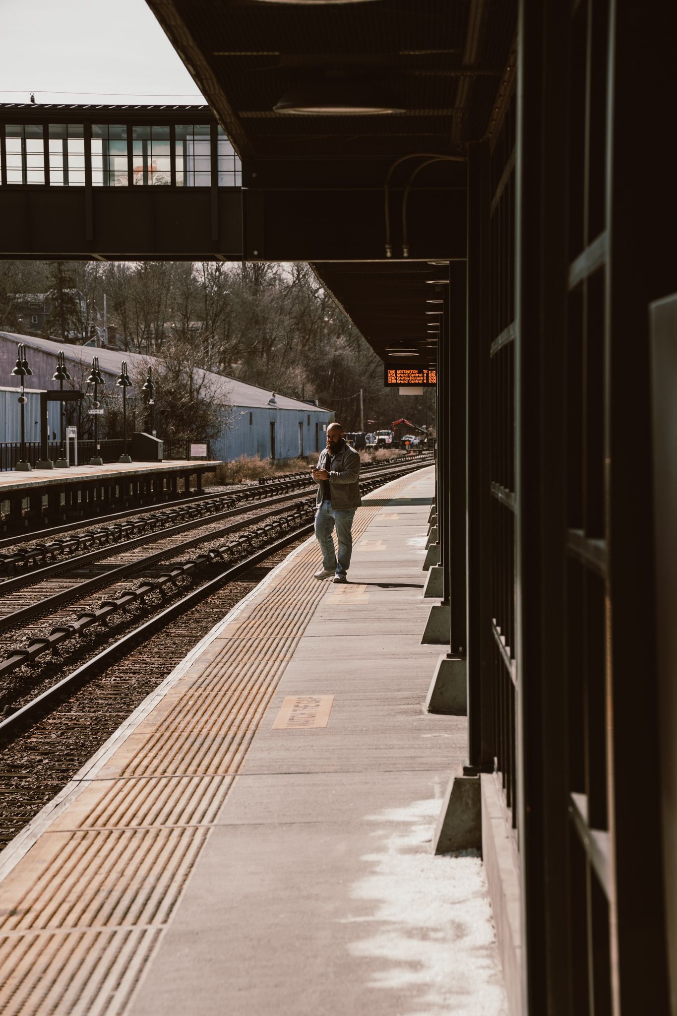 Lone passenger waiting on quiet commuter rail platform beside curved railroad tracks.