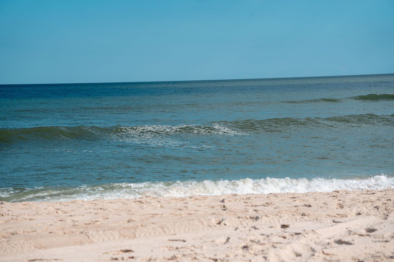 Calm ocean waves gently rolling onto a sandy beach under a clear blue sky.
