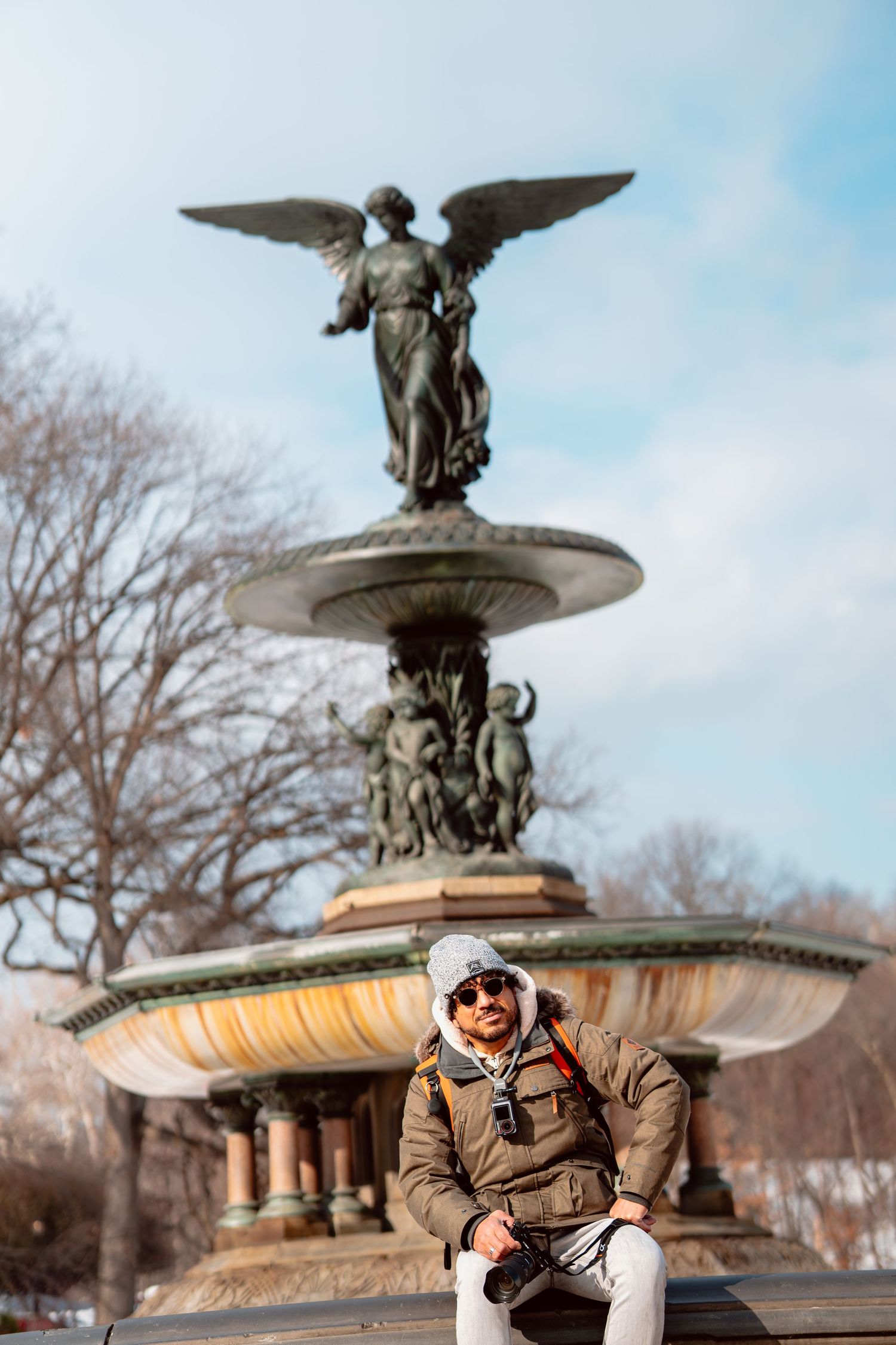Photographer sitting in front of Bethesda Fountain angel statue in Central Park during winter.