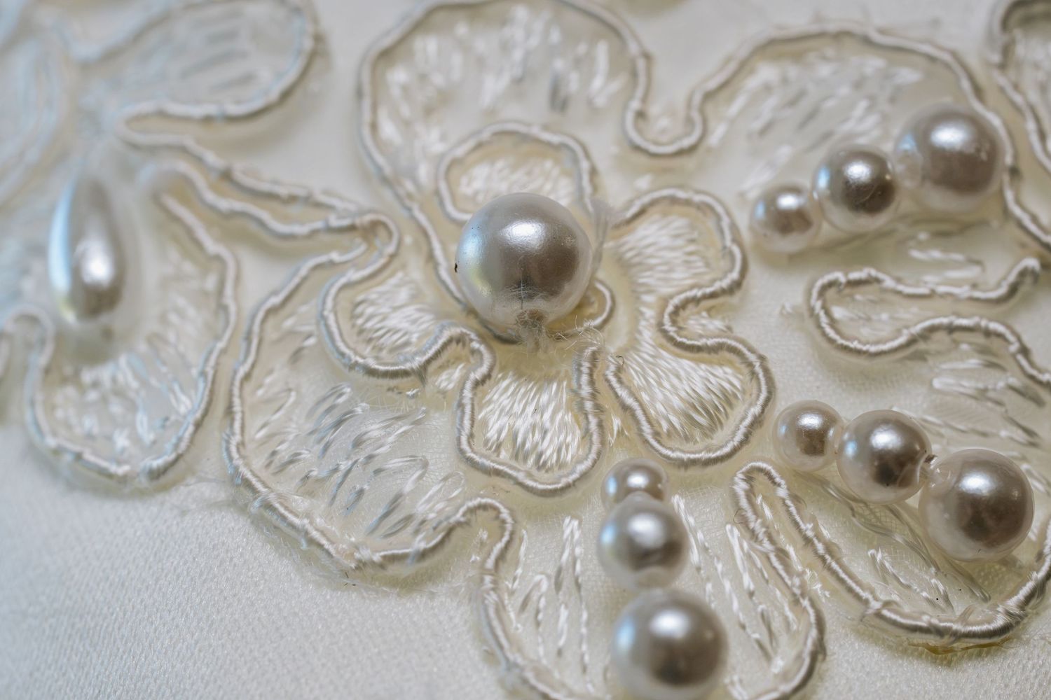 Close-up of ivory embroidered floral lace fabric adorned with lustrous silver-gray pearl beads.