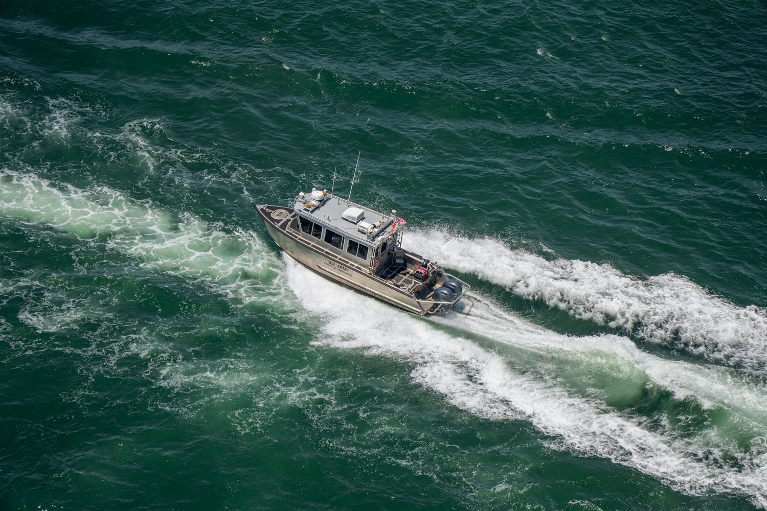 A small motorboat speeding through choppy green ocean waters, leaving a white wake trail behind it.