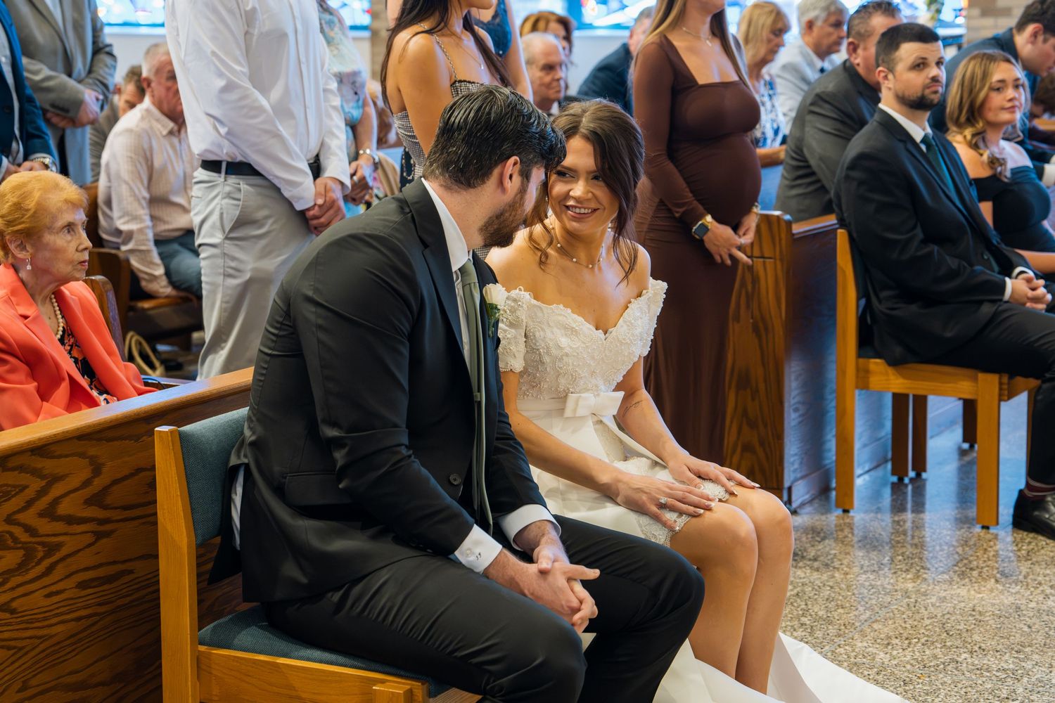Bride and groom share a joyful moment seated together during their wedding ceremony in a sunlit church.