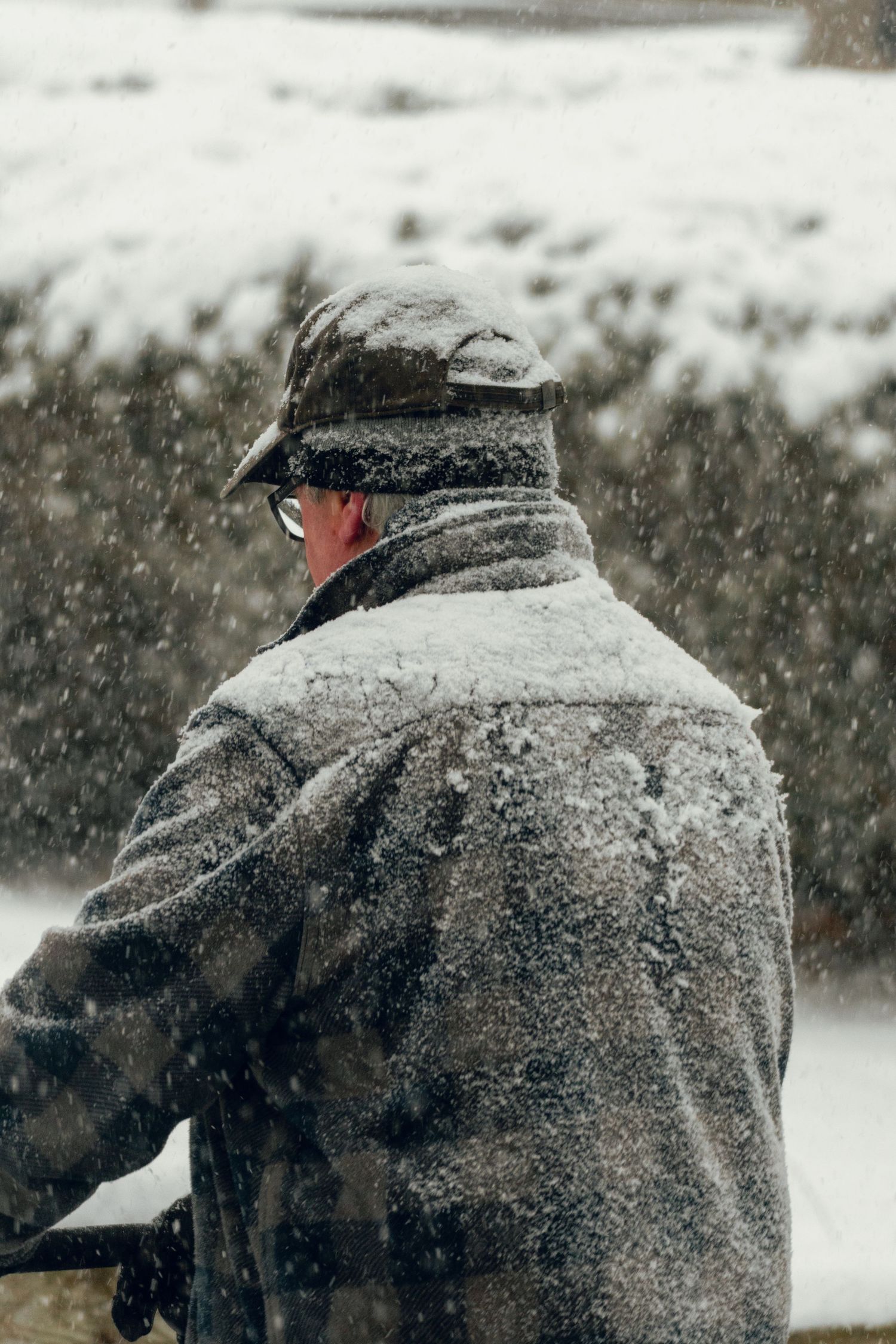 Rear view of a snow-covered man in a winter coat during a heavy snowstorm.