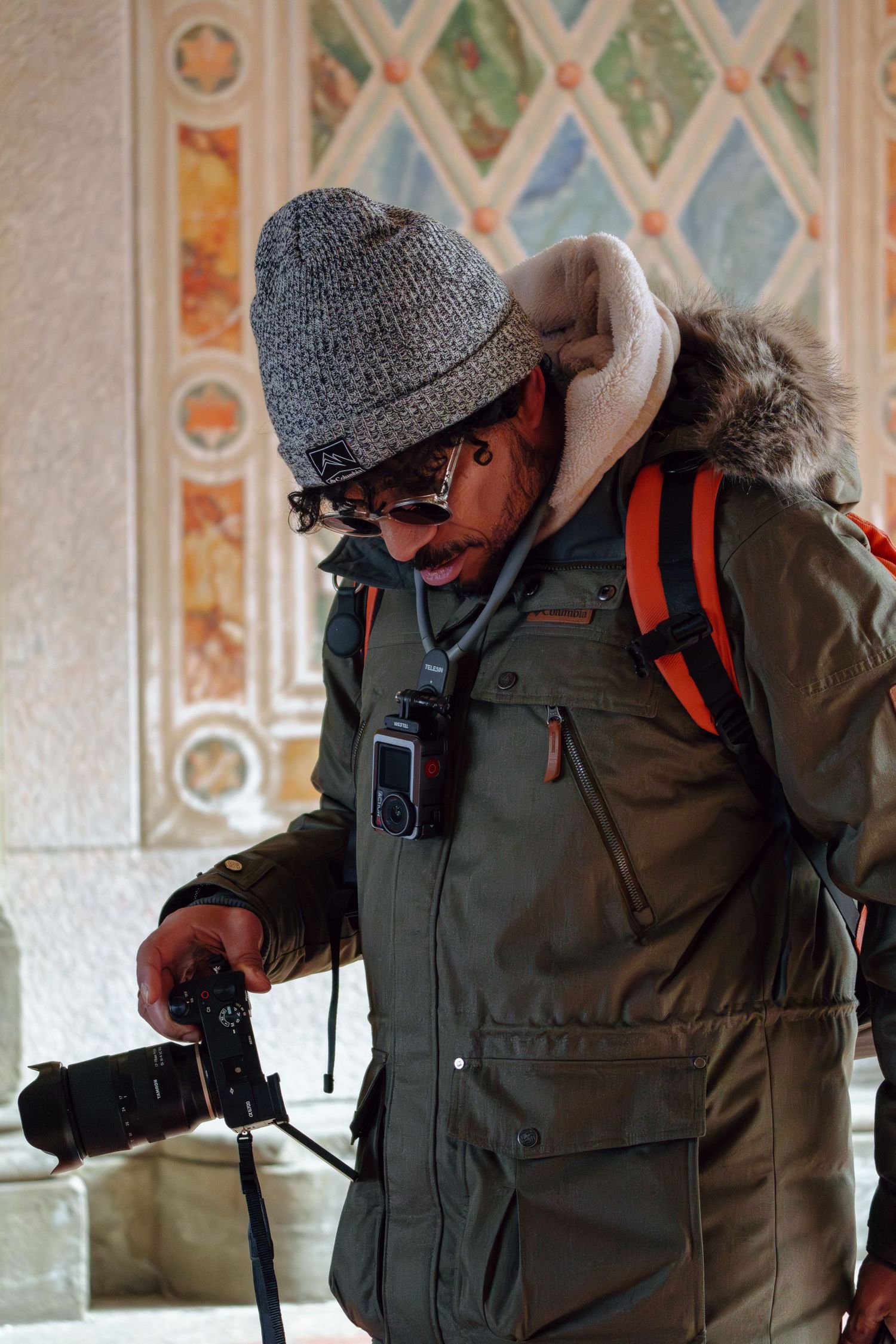 A photographer in a winter parka and knit hat reviews images on his camera inside Bethesda Terrace.