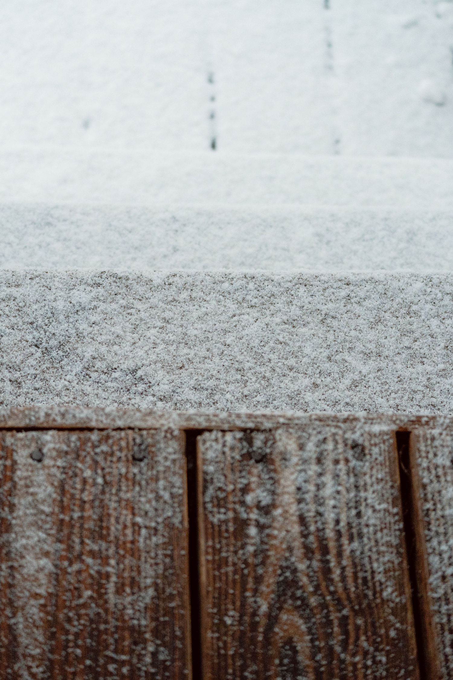 Delicate fresh snow resting on the edge of a weathered brown wooden deck.
