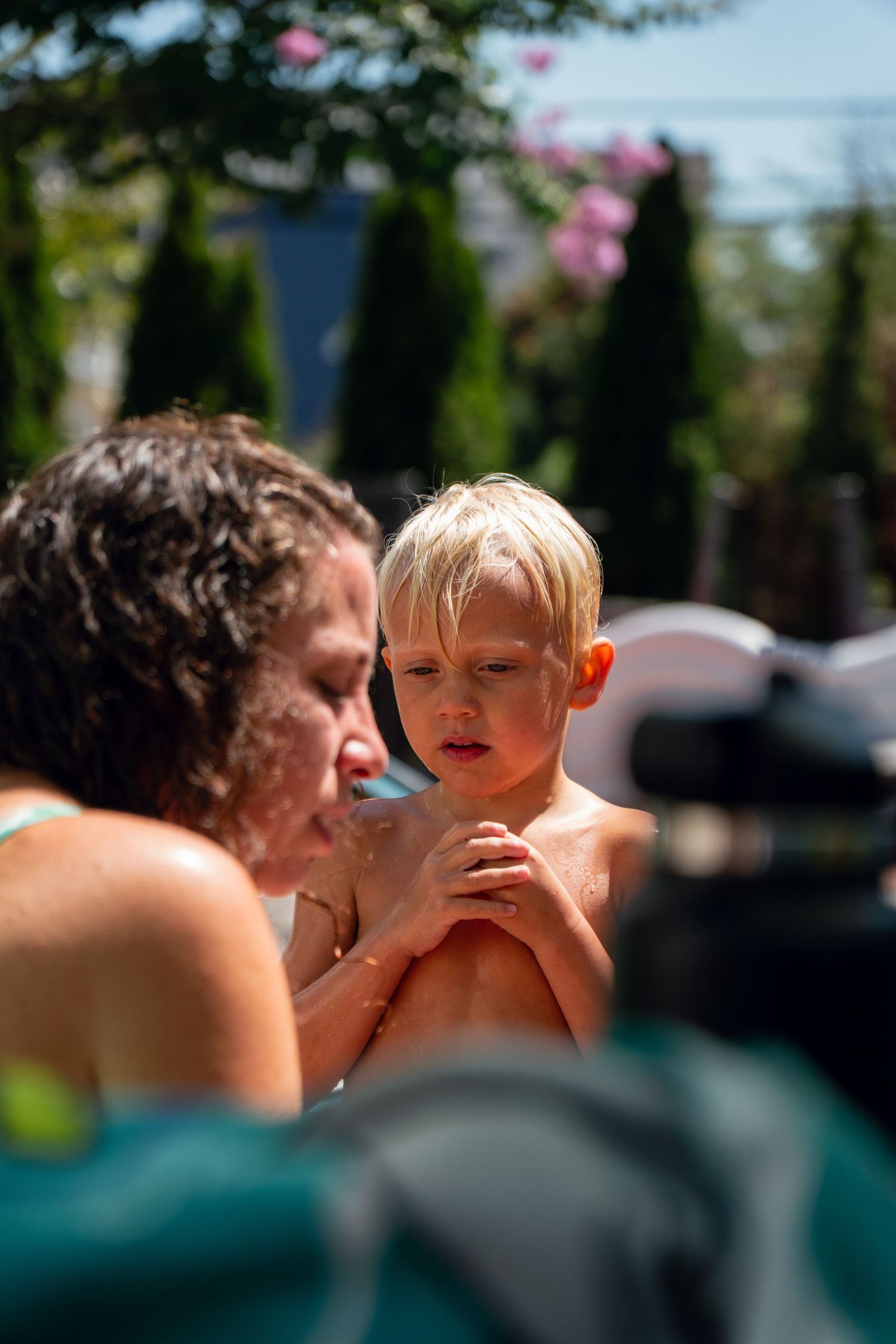 Mother applying sunscreen to young blonde boy poolside on a sunny summer day.