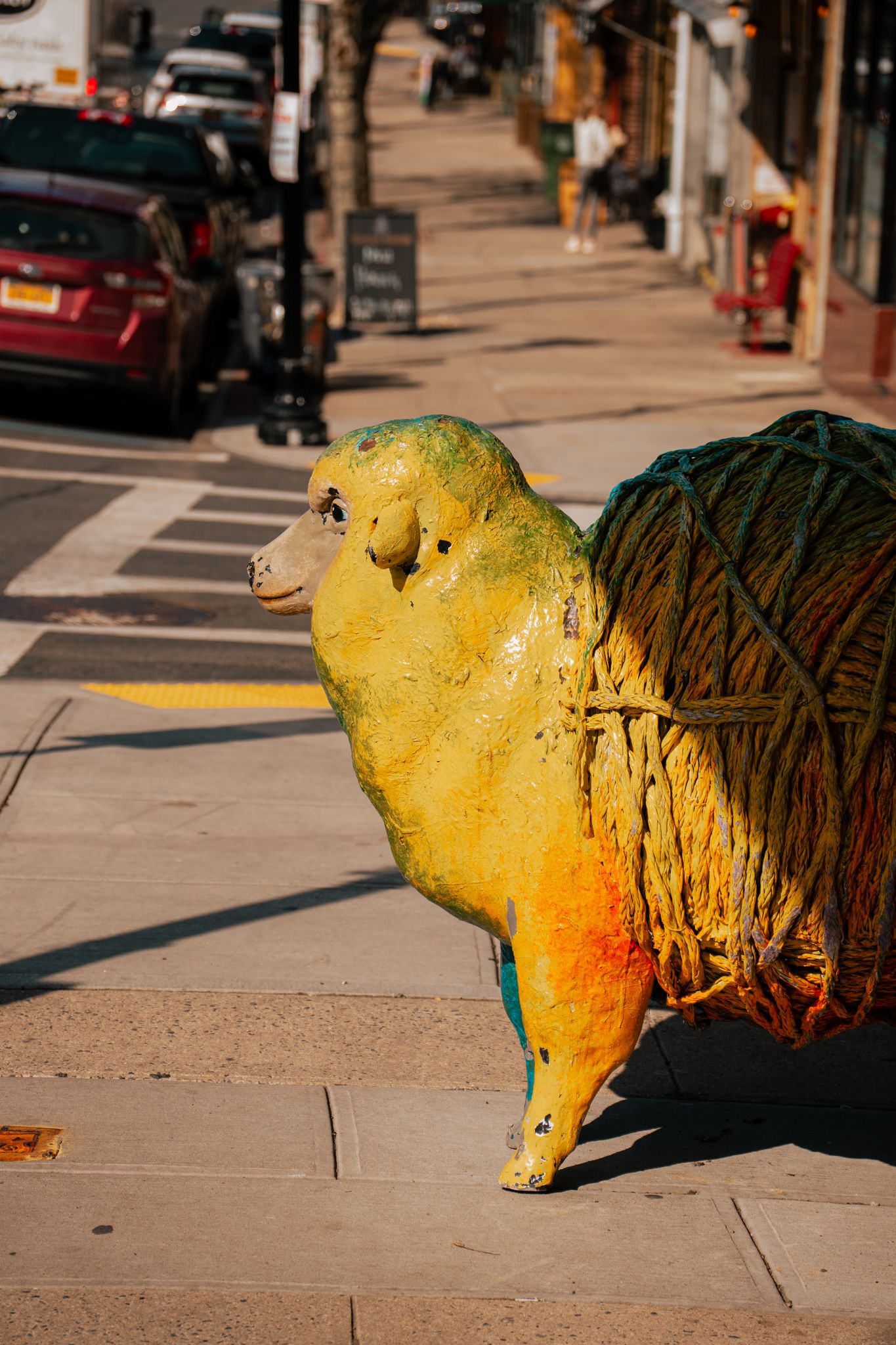 Colorful yellow and green sheep sculpture displayed on a sunny city sidewalk.