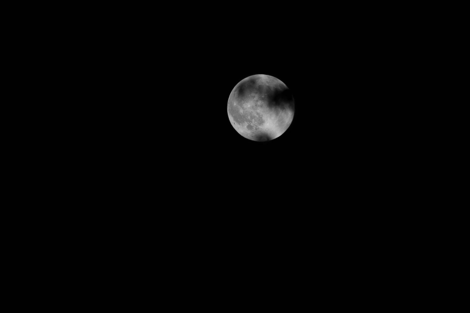 Partially shadowed full moon set against a pitch black night sky.