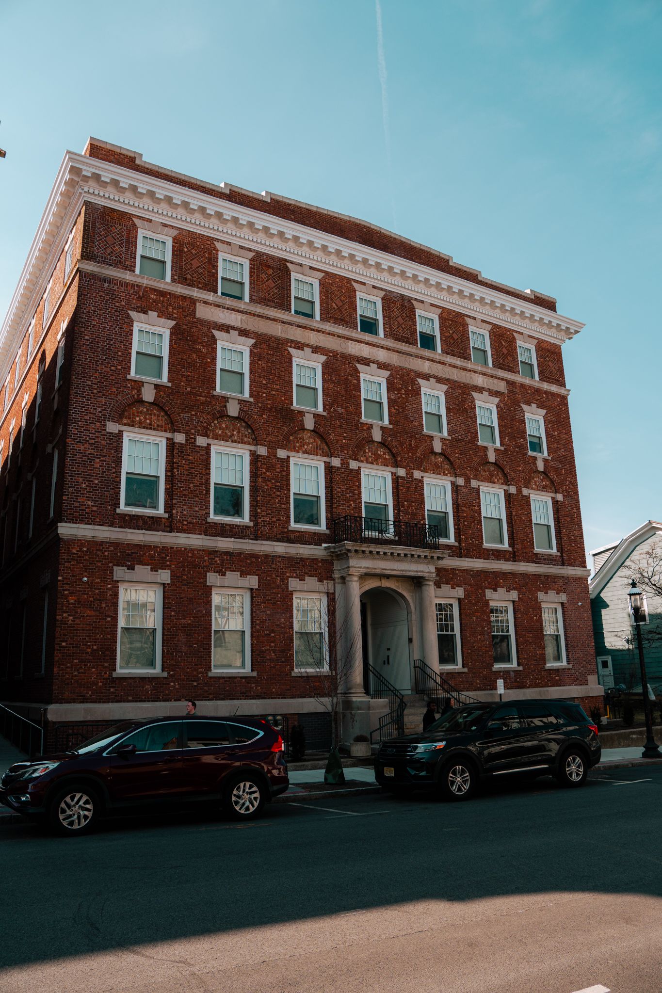 Historic four-story red brick apartment building with white trim under blue sky.
