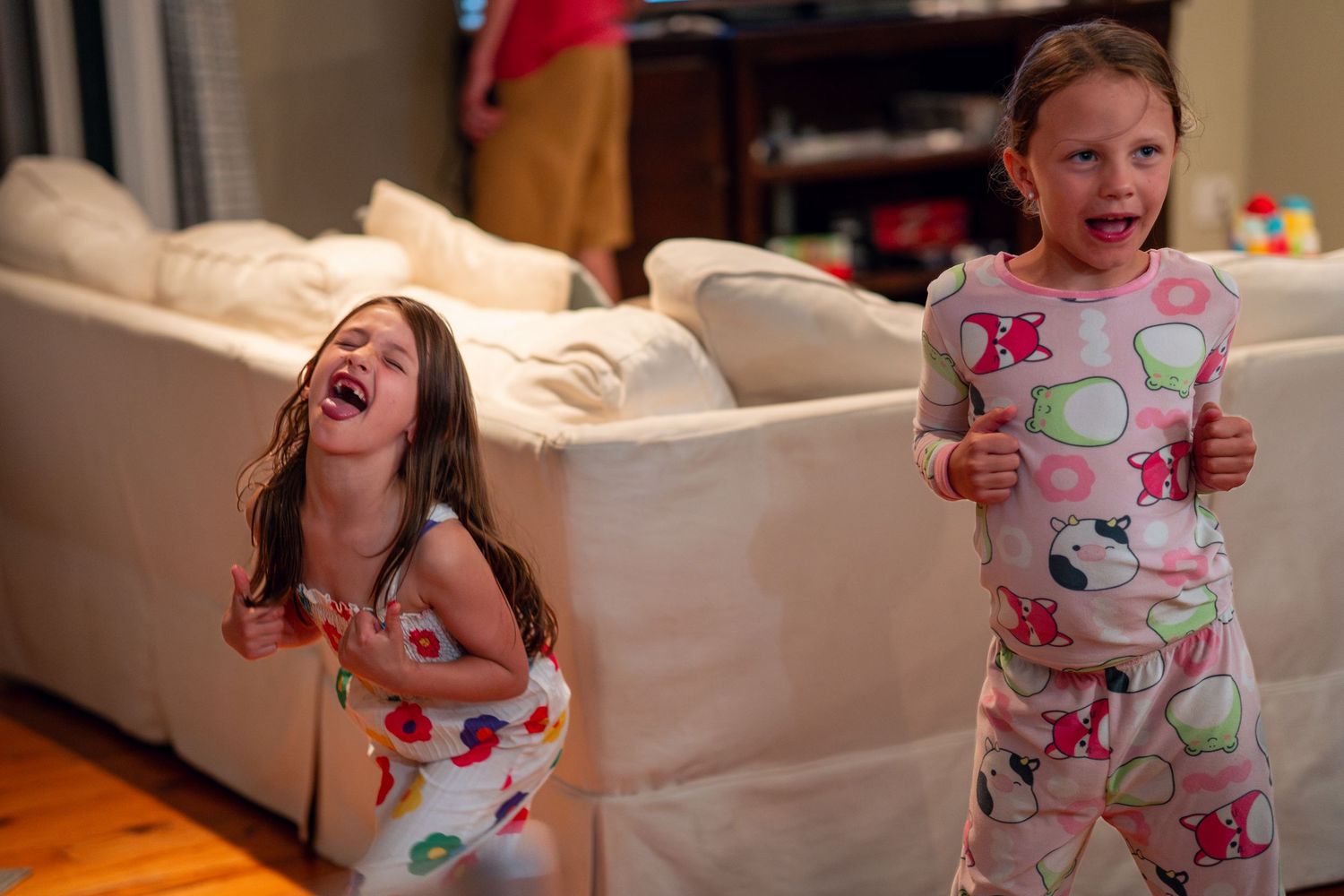 Two young girls in pajamas make silly faces and laugh together in a living room.