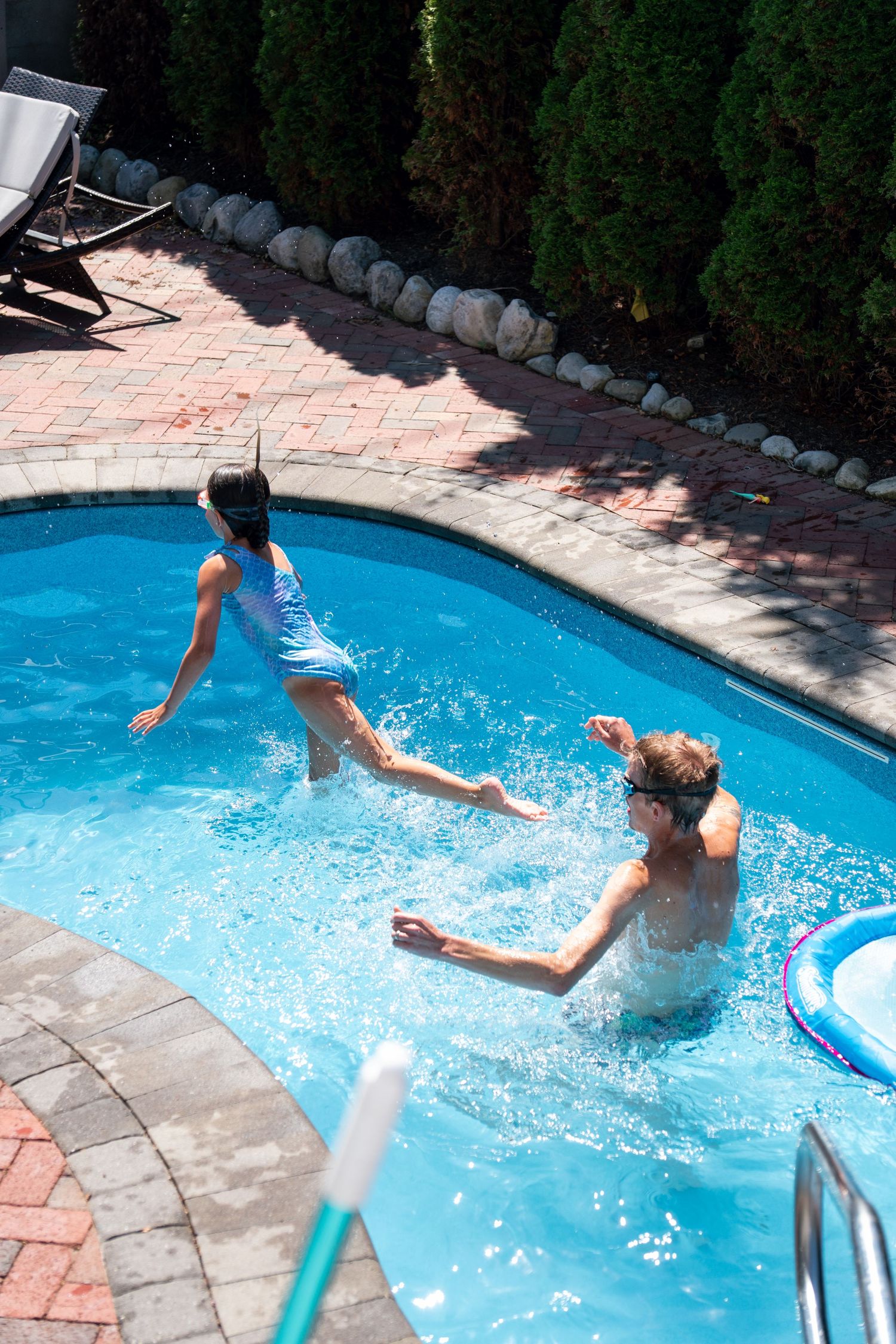 Child in blue swimsuit splashes into pool as adult reaches to catch her.