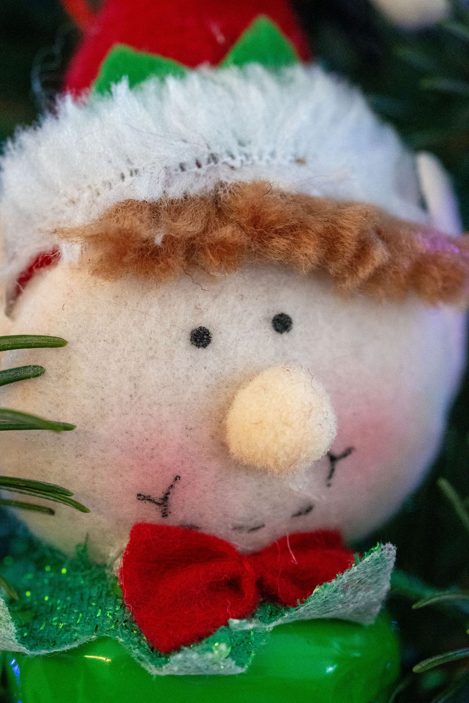 A cute plush elf Christmas ornament with a red bow tie and fluffy white hat.