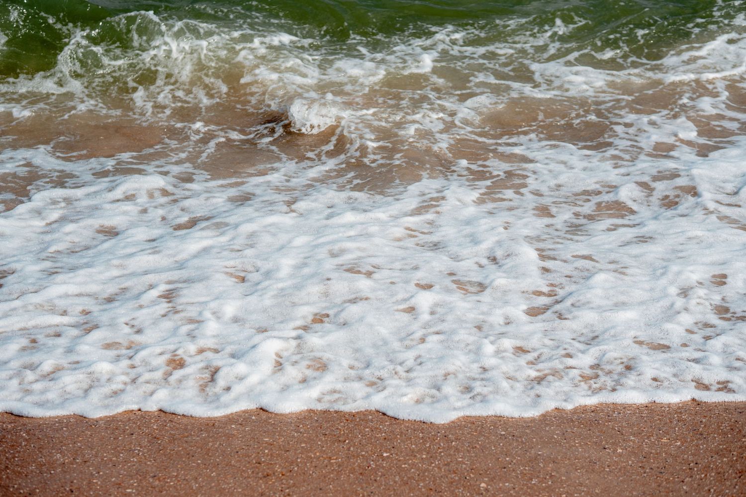 Foamy ocean waves washing over a sandy brown beach shoreline close-up view.