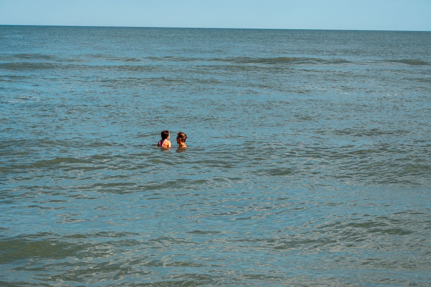 Two people swimming together in the vast open ocean on a clear sunny day.
