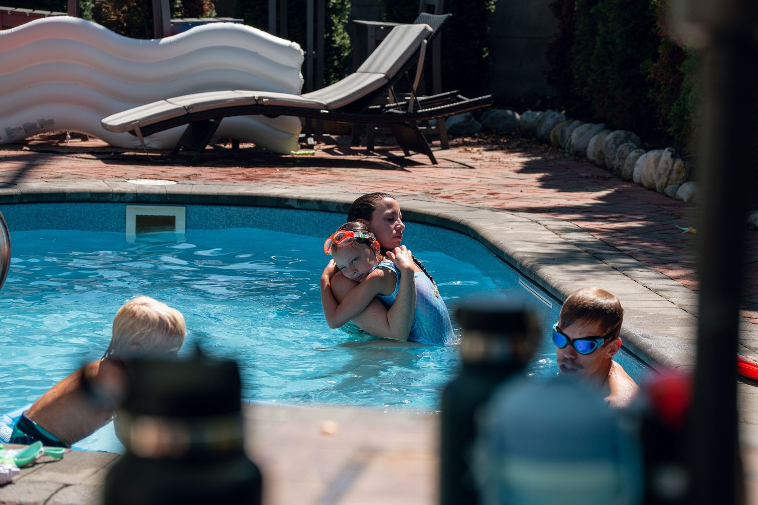 Adults and children enjoying a sunny day swimming in a backyard pool.
