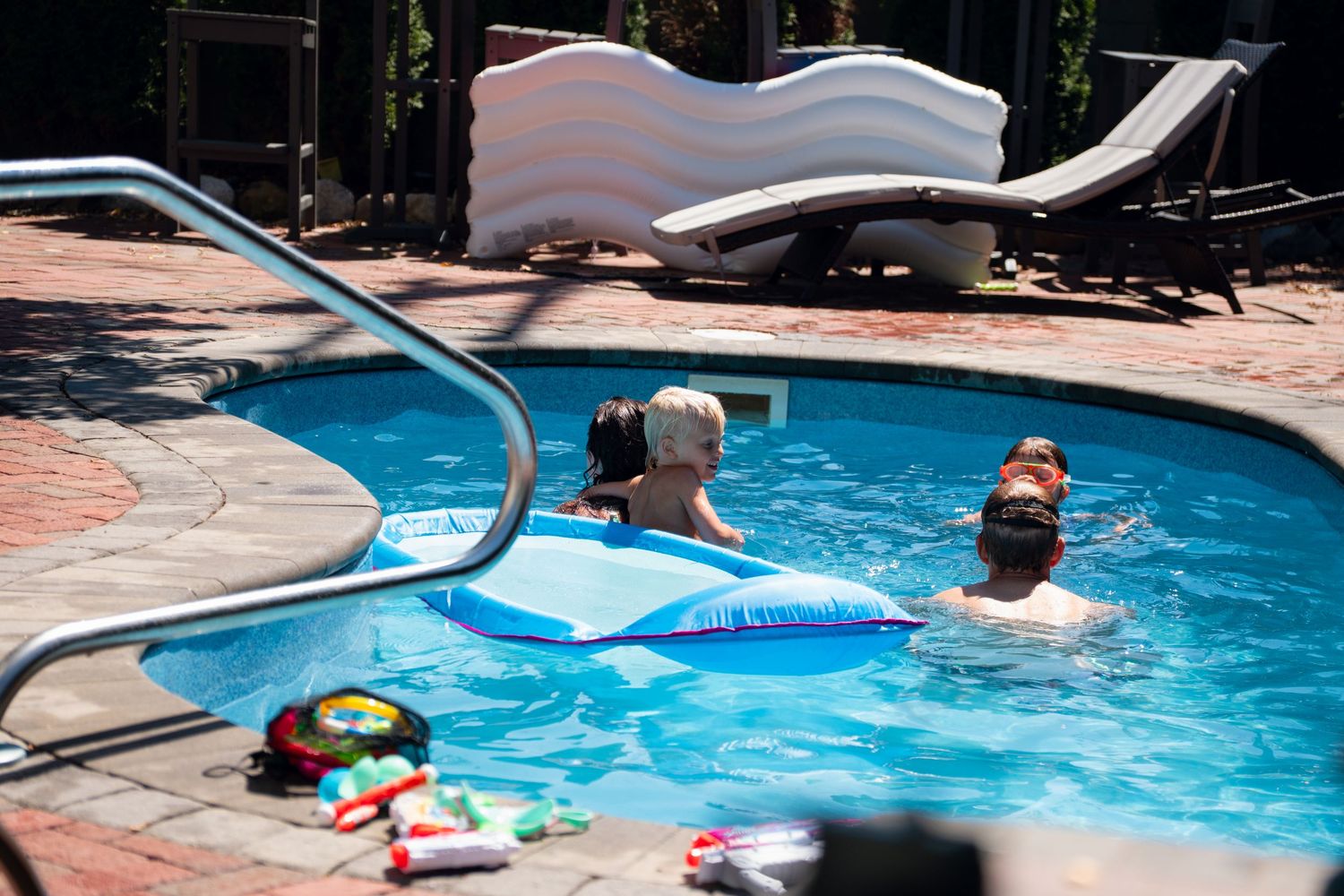 Two children swim with blue inflatable float in sunny backyard swimming pool.