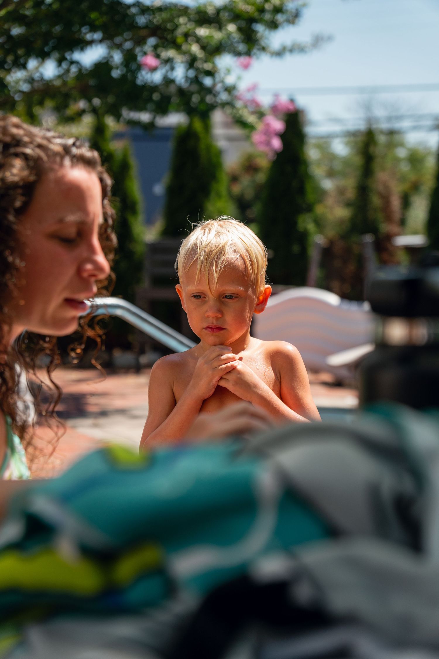 Woman tending to a young blonde boy with crossed arms near a backyard swimming pool.