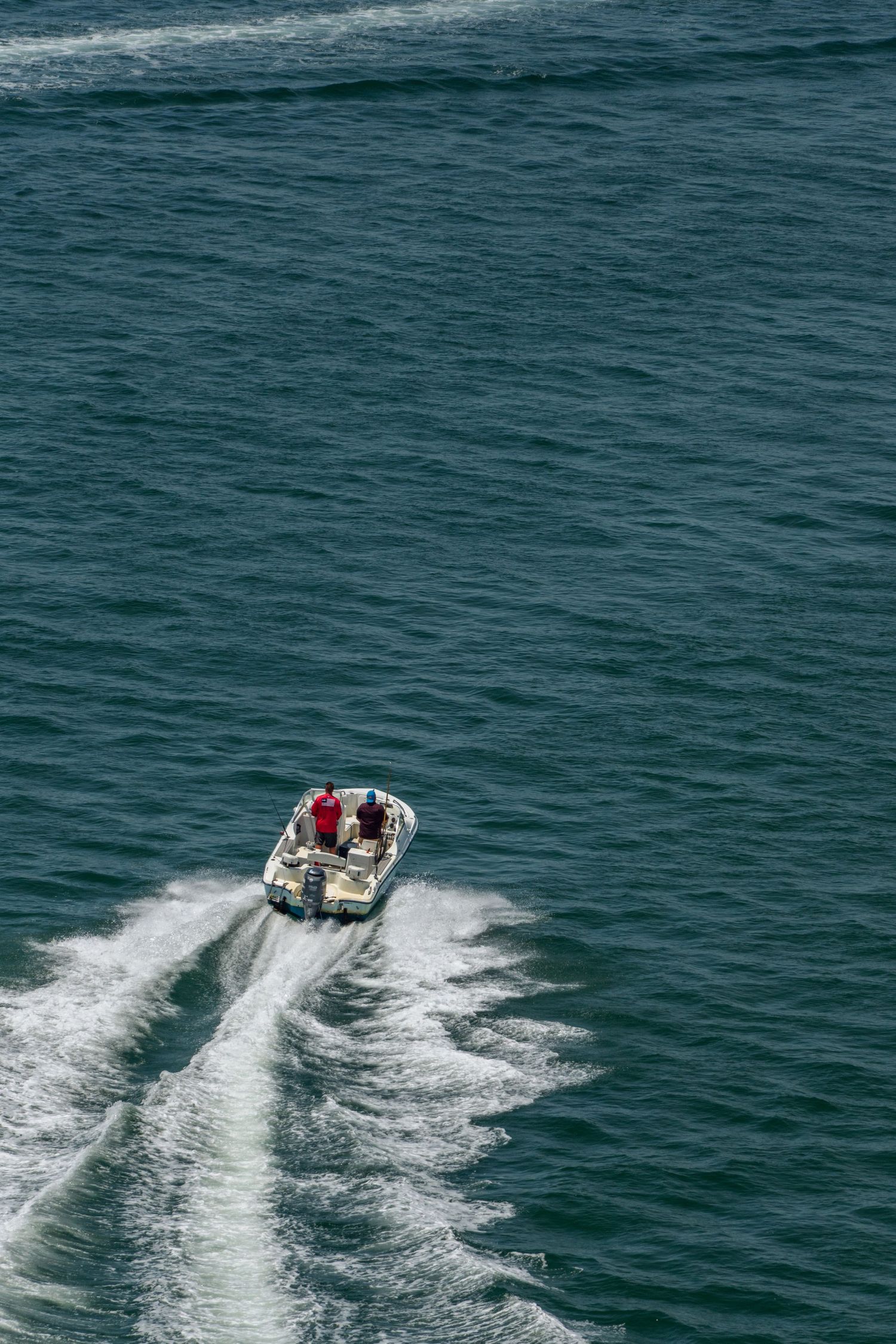 Two people riding a speedboat on turquoise ocean waters, leaving a white wake trail behind them.