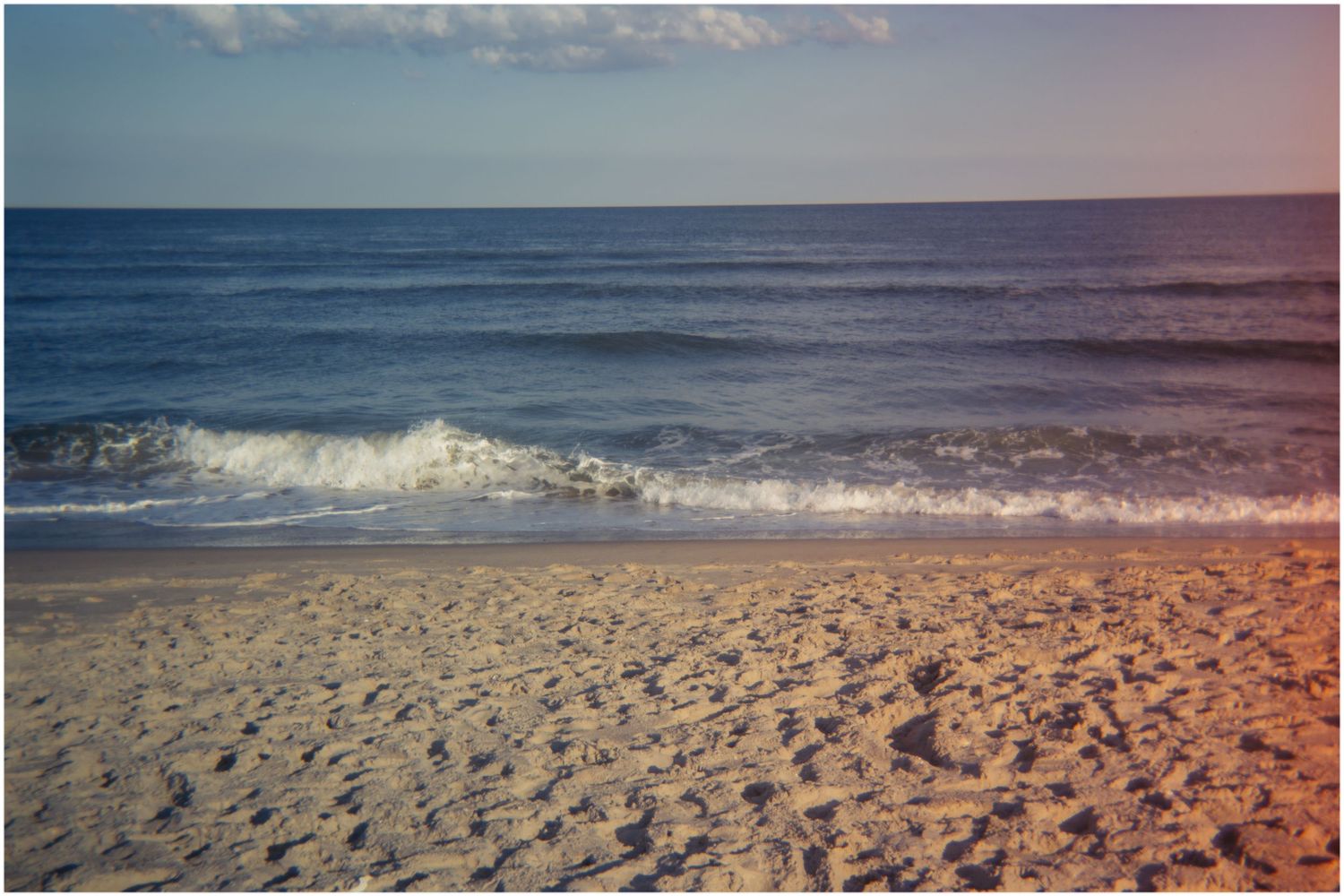Warm sunset light illuminating a sandy beach with gentle ocean waves and a blue horizon.