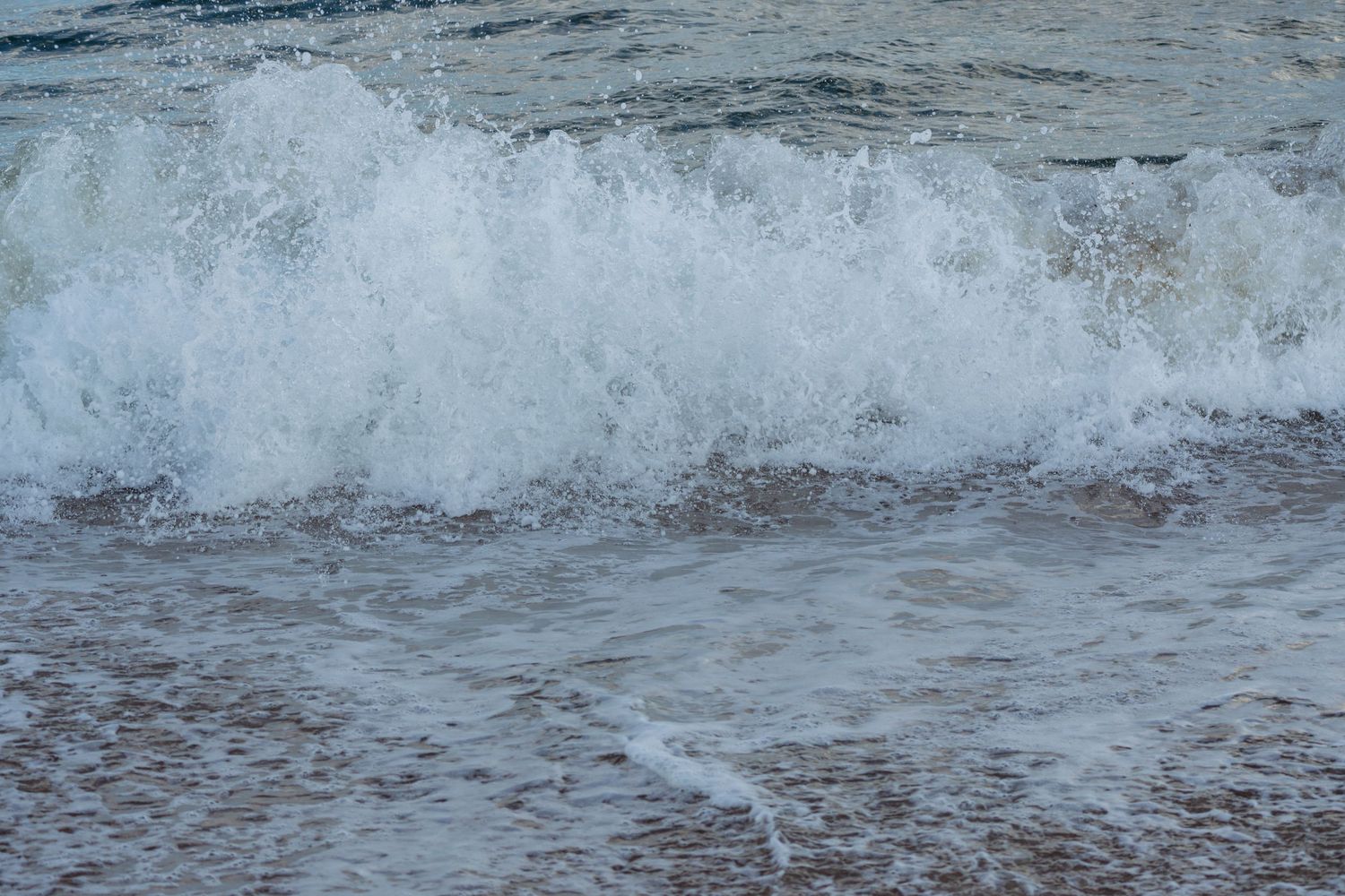 A powerful white-capped ocean wave breaking and splashing onto the sandy shore.