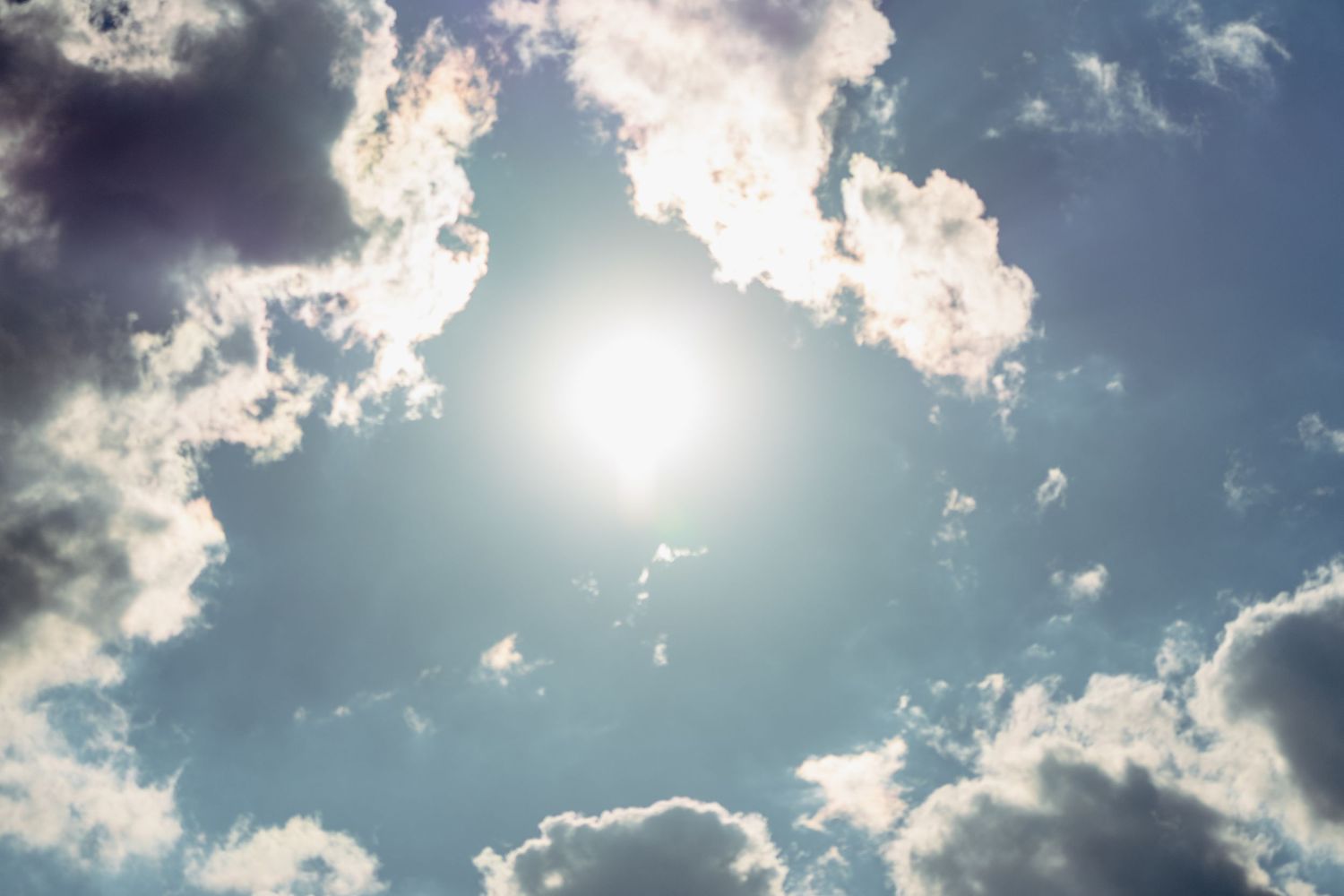 Bright sun shines through dramatic white clouds in a vivid blue sky.