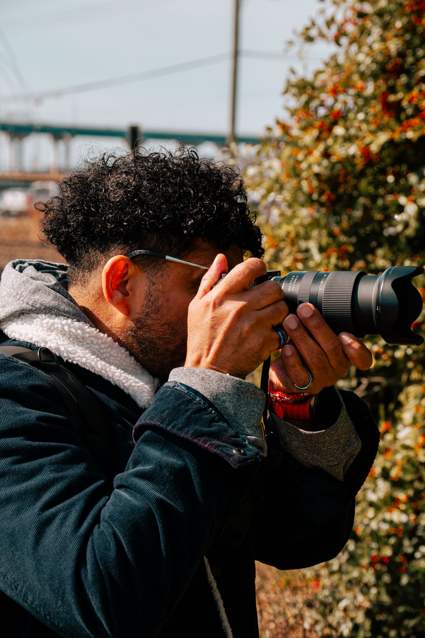 Curly-haired photographer with sunglasses capturing photos with a telephoto lens outdoors.