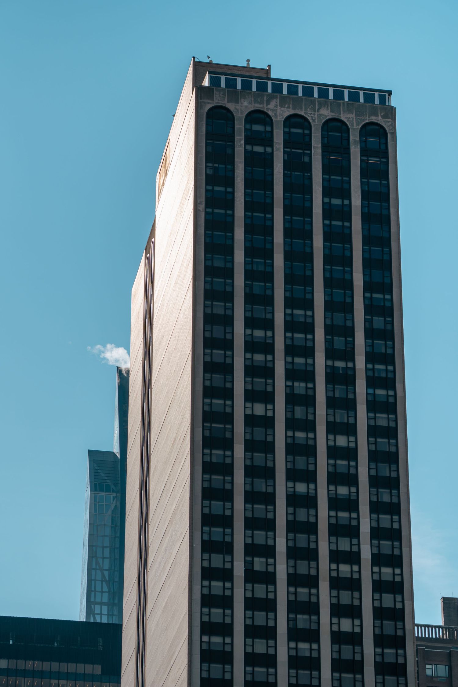 Tall brutalist office building with arched windows against a bright blue sky.