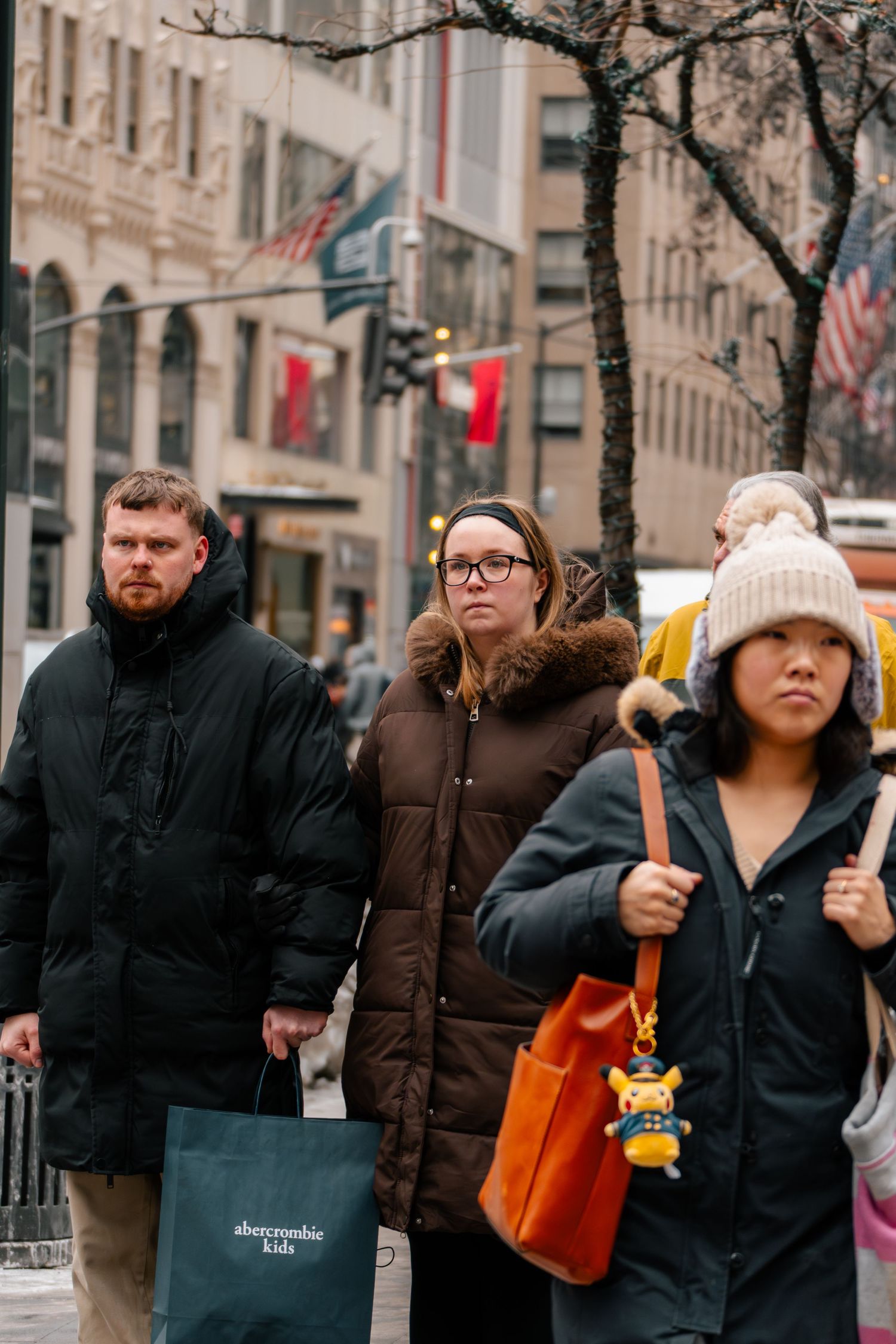 Shoppers in winter coats walking along a busy New York City street carrying Abercrombie Kids shopping bags.