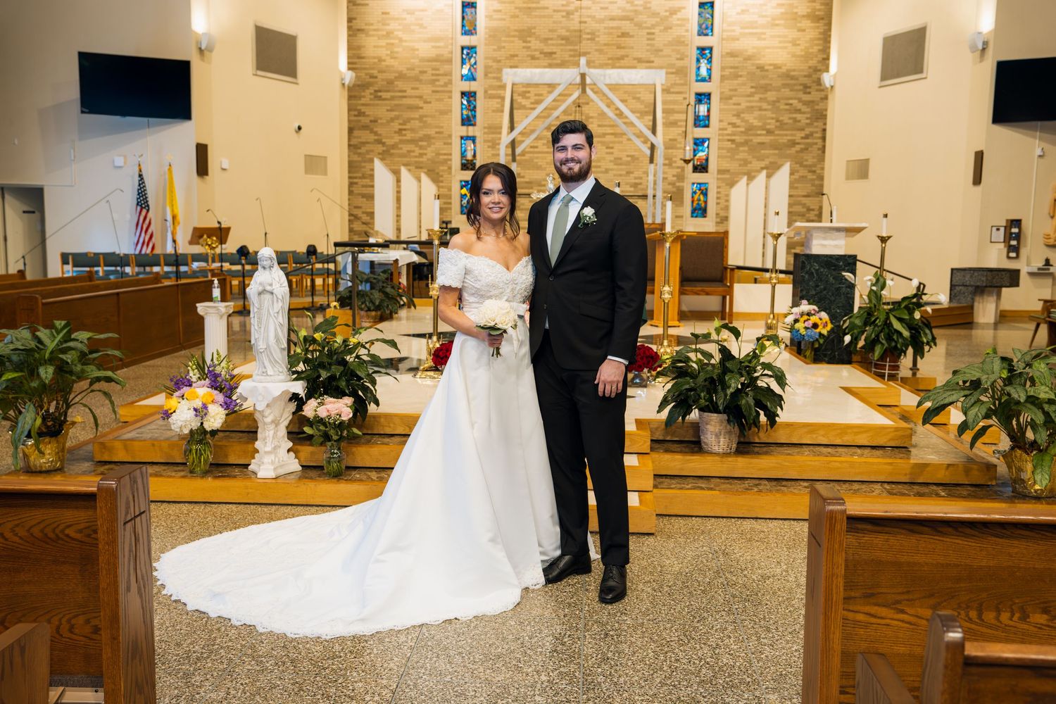 Bride and groom posing together at the altar of a decorated Catholic church on their wedding day.