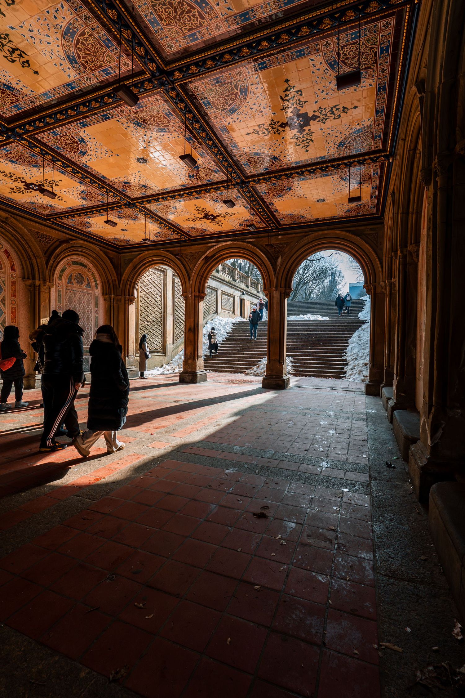 Sunlight streams through arches of Bethesda Terrace underpass with ornate tiled ceiling in Central Park.